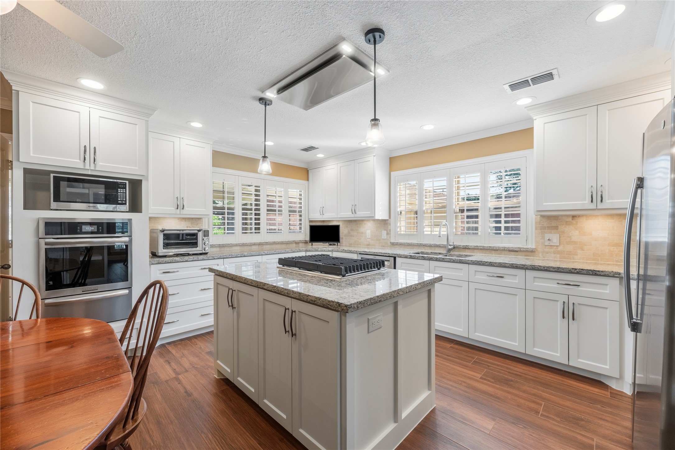 Gorgeous island kitchen features granite countertops, white cabinetry, under cabinet lighting, tile backsplash, stainless steel appliances and a gas cooktop.