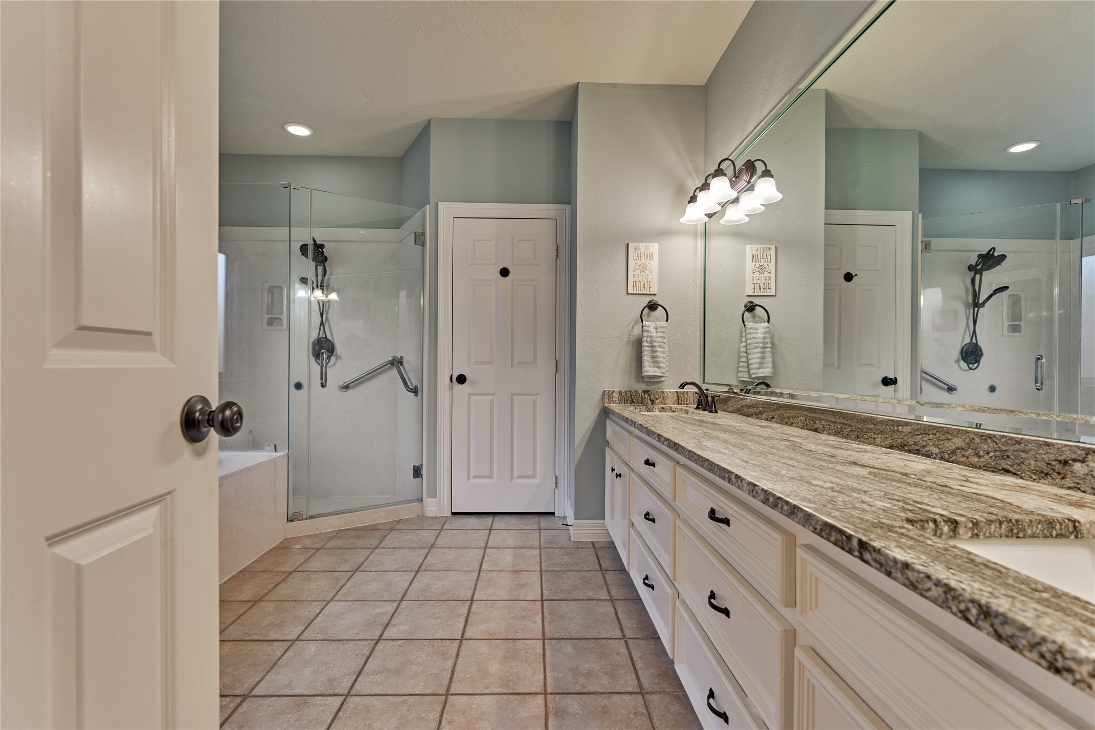 Updated spa-inspired ensuite bath featuring dual vanities, granite countertops, a relaxing soaking tub, and a frameless walk-in shower.