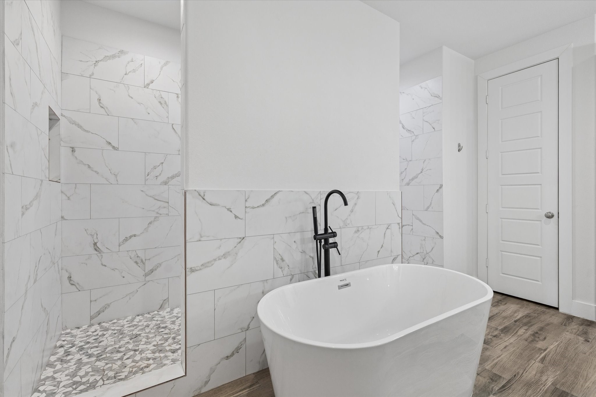 The elegant and modern bathtub is perfect for relaxing and recharging after a long day. The space showcases sophisticated design details, including wall tile colors that harmonize beautifully with the marble surfaces. The black faucet on the tub provides a striking contrast to the light color palette, while the spacious shower behind the tub and the attention to flooring details complete this unique and visually stunning bathroom. The surfaces are also easy to clean, combining style with functionality.
