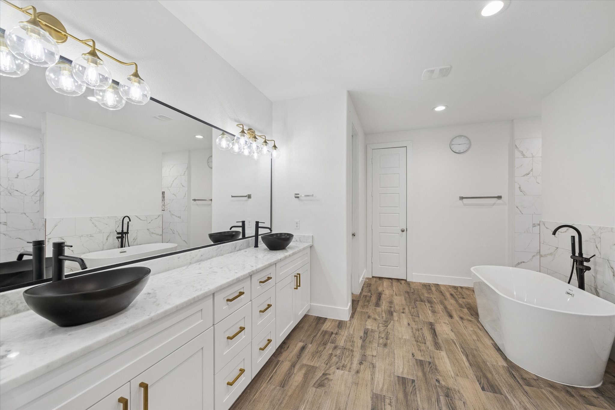 This ensuite bathroom showcases elegance and thoughtful design in every detail. The marble countertops, custom mirrors, and brass LED light fixtures create a sophisticated, harmonious look. Recently installed dark sinks and black faucets add striking contrast while enhancing the overall aesthetic, making this space both functional and exceptionally refined.