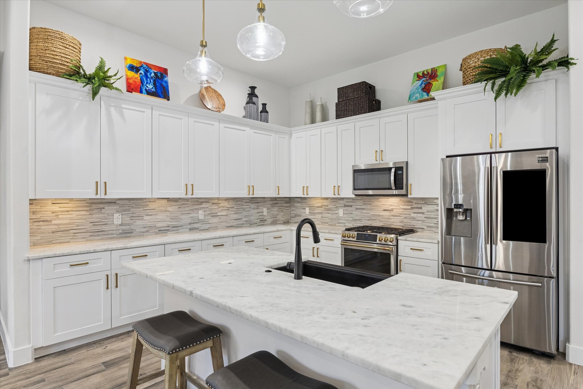 A dream kitchen with a spacious layout and elegant touches, including marble countertops and new brushed brass pulls on all cabinets. The Cafe Gas Dual Fuel Range with dual ovens and Wi-Fi-enabled oven is perfect for cooking enthusiasts, making meal preparation and entertaining effortless. The harmonious color palette creates a sense of elegance, calm, and inspiration, ideal for cooking, enjoying coffee, and creating memorable moments with family and friends.