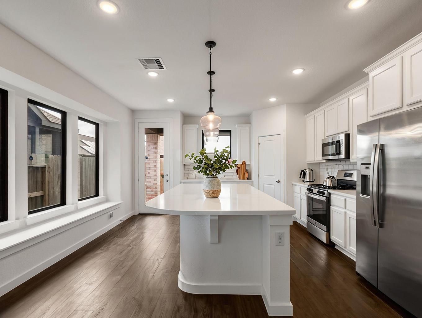 This kitchen angle showcases the island as the centerpiece of the home. Clean counters, warm flooring, and white cabinetry create a sharp, balanced look. Virtually staged.