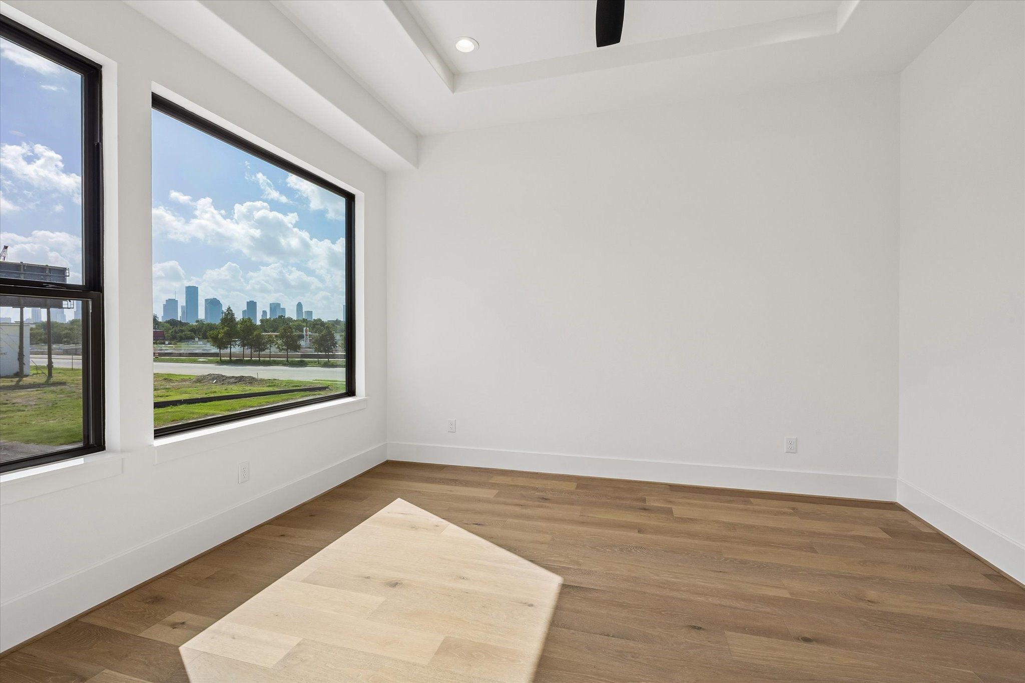 Downtown skyline views become a standout feature of this secondary bedroom, framed by oversized black windows. A tray ceiling and hardwood floors carry the homes clean, contemporary design upstairs.