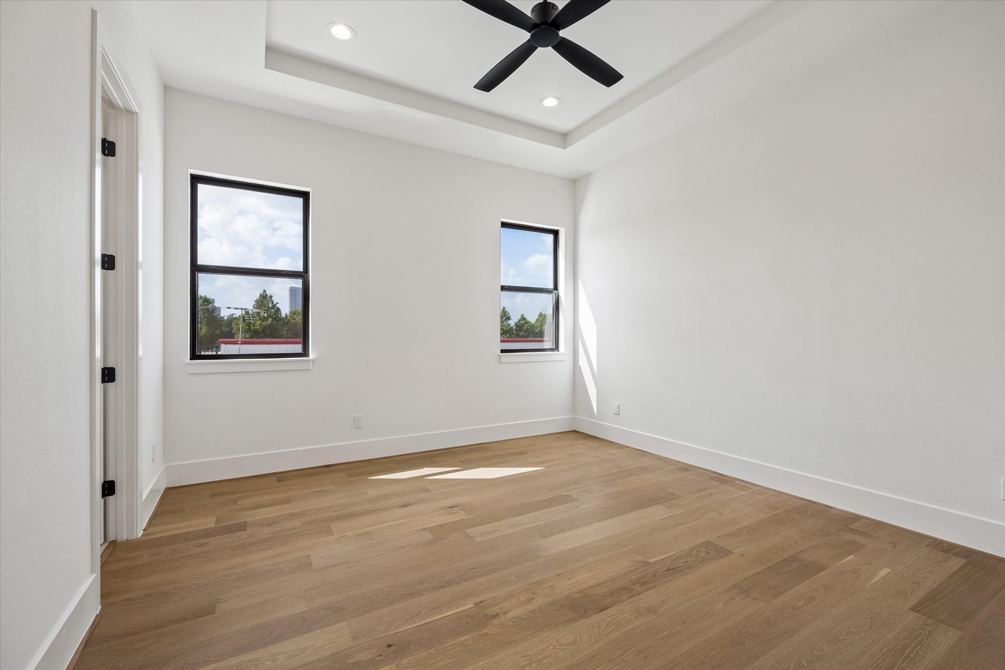 Clean lines and a tray ceiling give this secondary bedroom a polished architectural feel, while two black framed windows bring in natural light and elevated neighborhood views.
