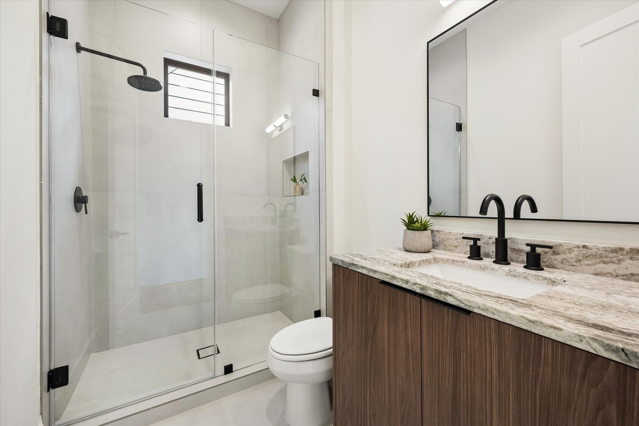 Serving both a secondary bedroom and the loft, this hall bath features a glass enclosed walk in shower, warm wood vanity, stone countertop and matte black fixtures for a crisp, modern finish.