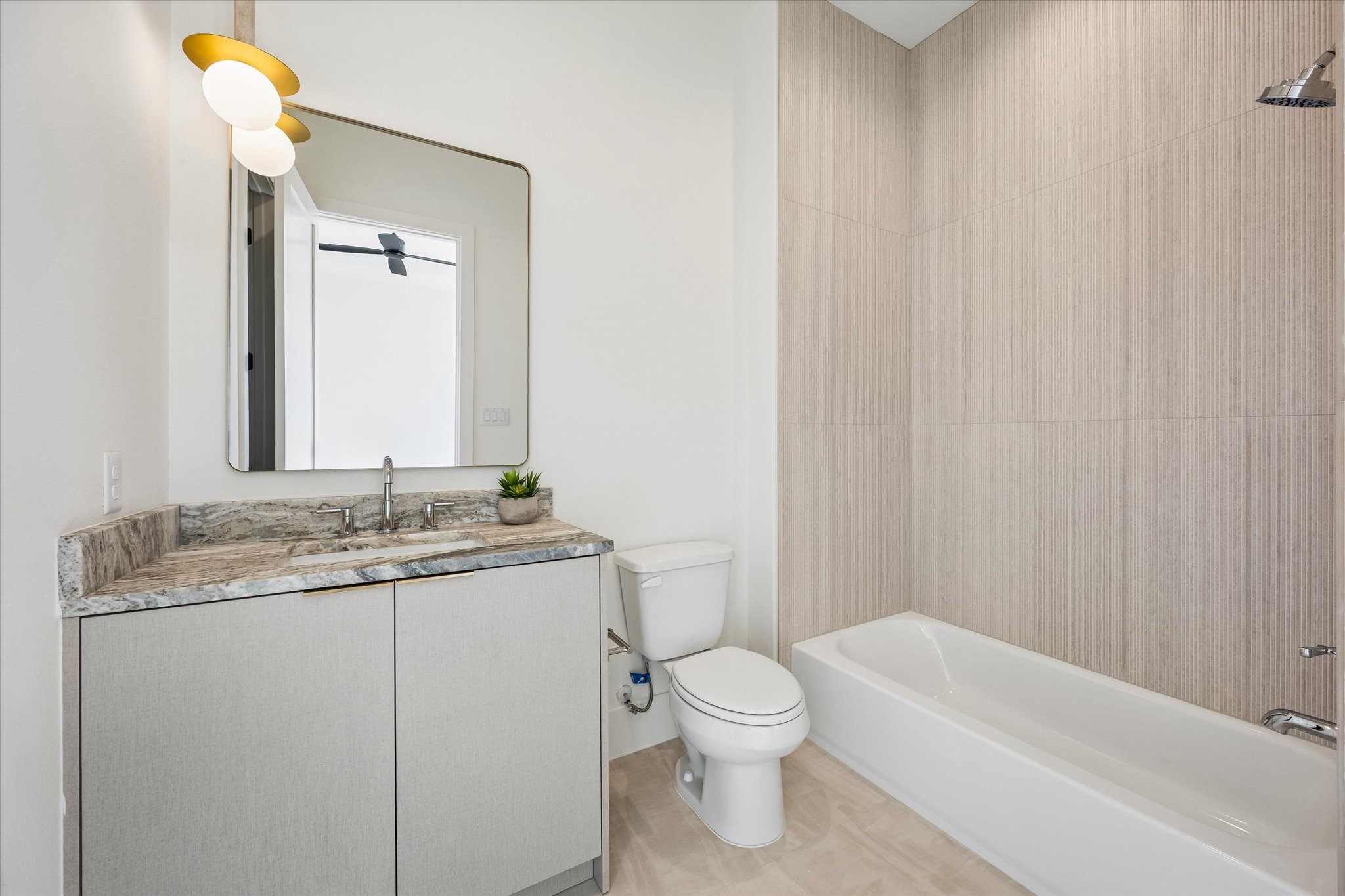 Private ensuite bath complements the secondary bedroom with a stone topped vanity, streamlined cabinetry and full tub and shower combination wrapped in textured tile.