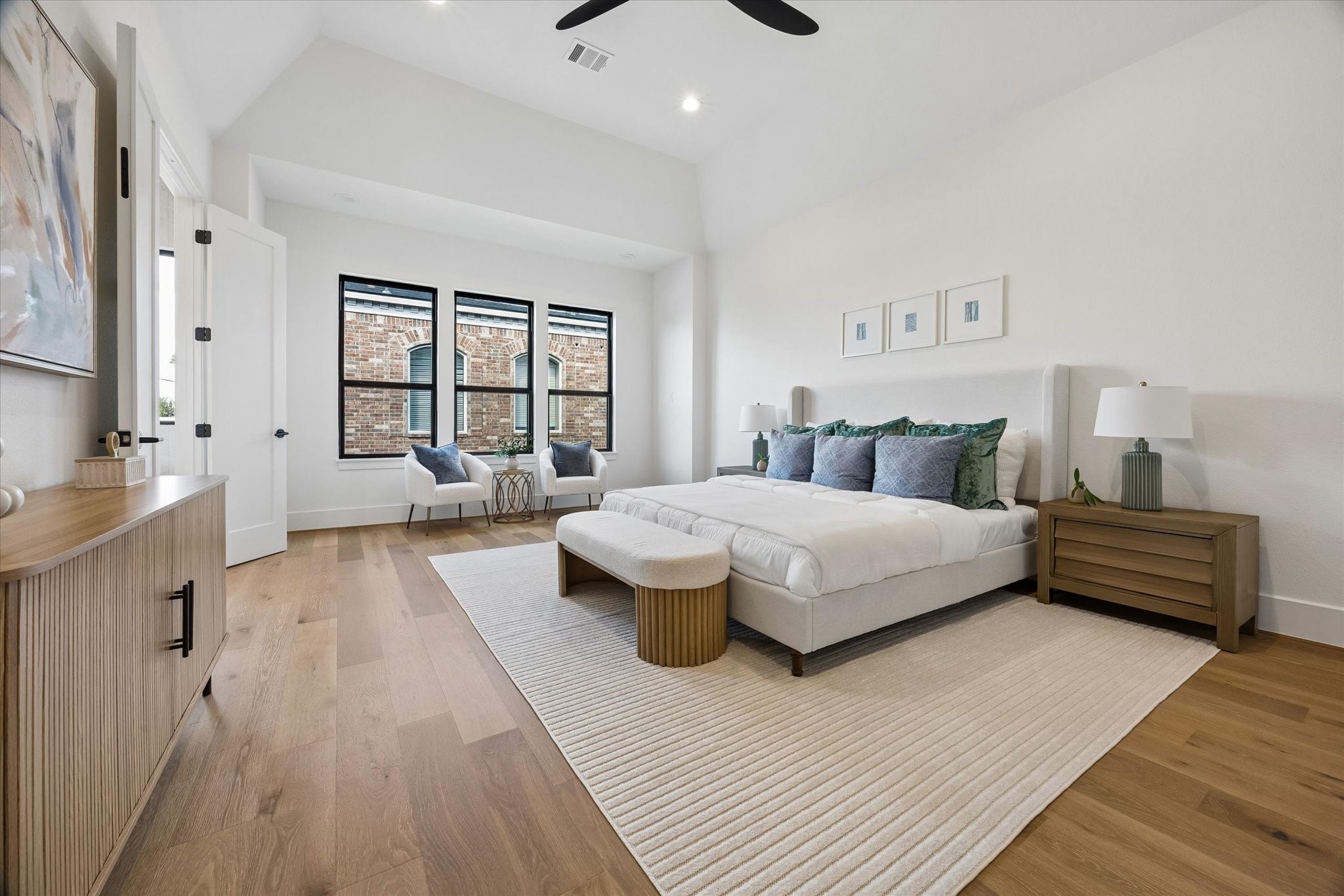 Vaulted ceilings give the primary suite an airy sense of scale, while a trio of black framed windows brings in natural light. Hardwood floors continue into the retreat for a cohesive finish.