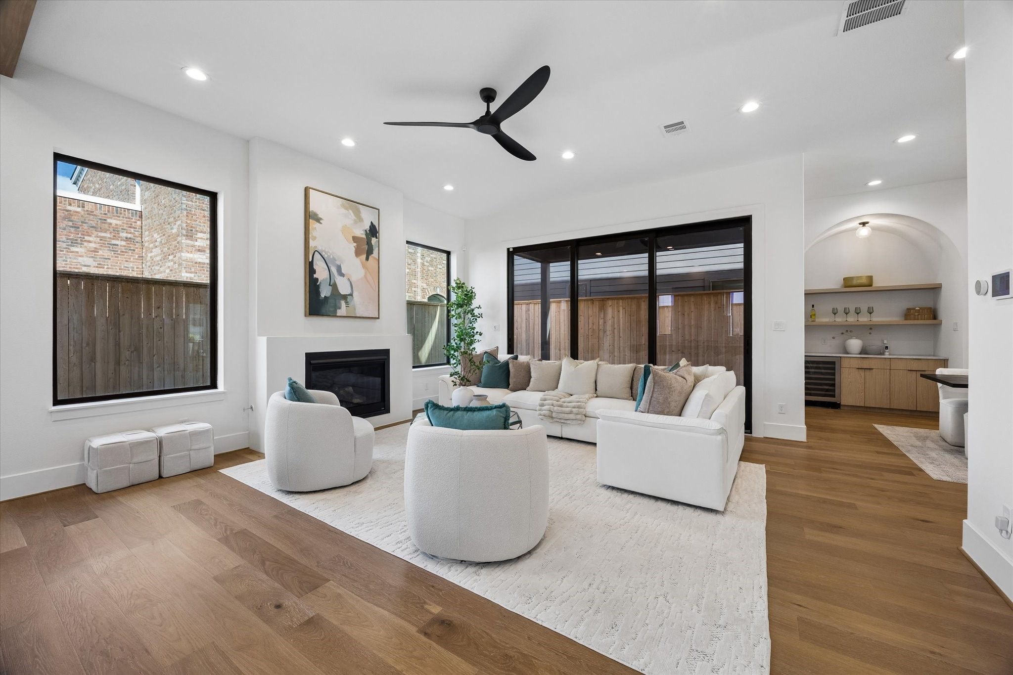 Soaring ceilings and oversized windows give the living room a bright, expansive feel, while the sleek fireplace adds a clean focal point. Large sliding glass doors create a strong indoor outdoor connection and extend everyday living toward the covered patio.