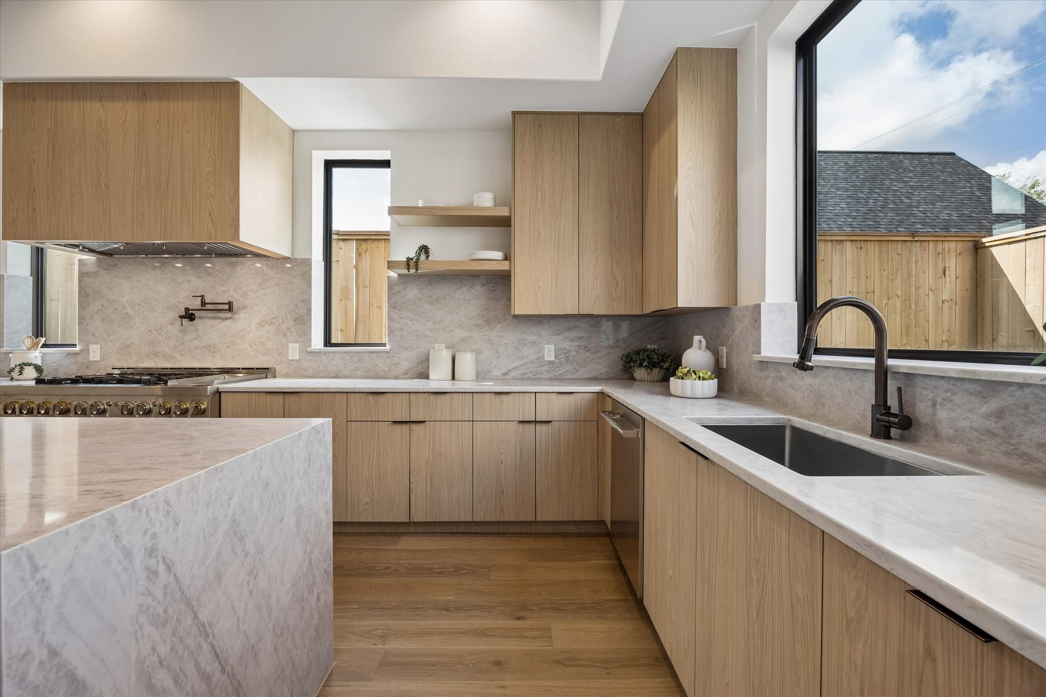 Thoughtful cabinetry extends around the kitchen to maximize storage while maintaining the clean, minimalist aesthetic. Open shelving, an undermount sink and expansive picture window add warmth and natural light to the workspace.