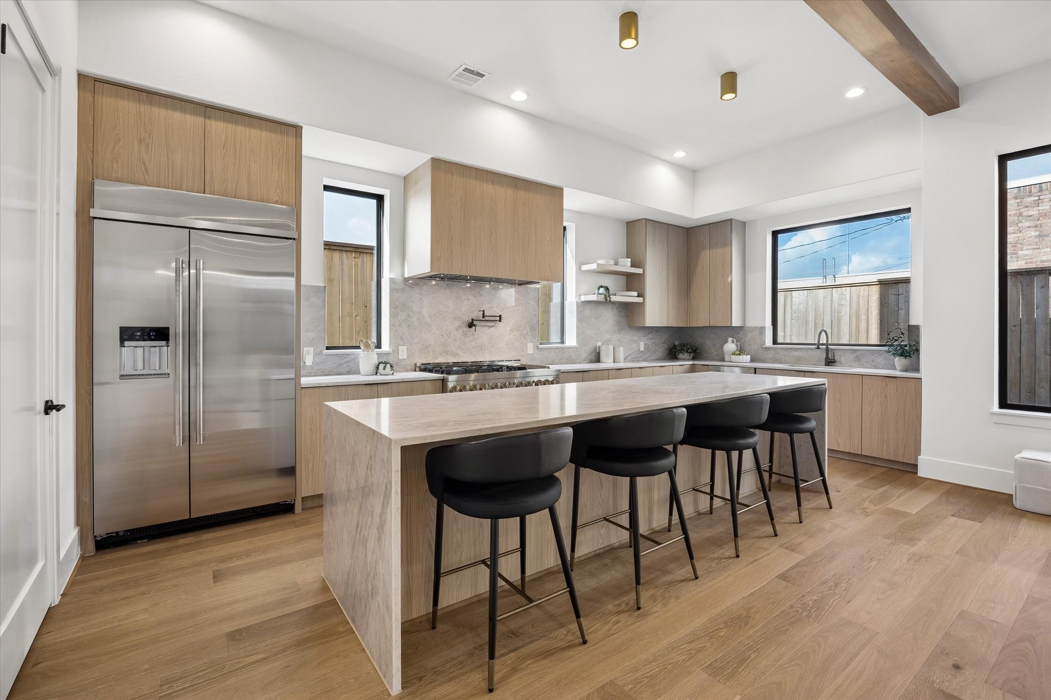 Generous proportions make the kitchen equally suited to everyday meals and entertaining, with an oversized waterfall island, abundant cabinetry and professional style appliances. Warm wood tones and brass ceiling accents soften the clean, modern palette.