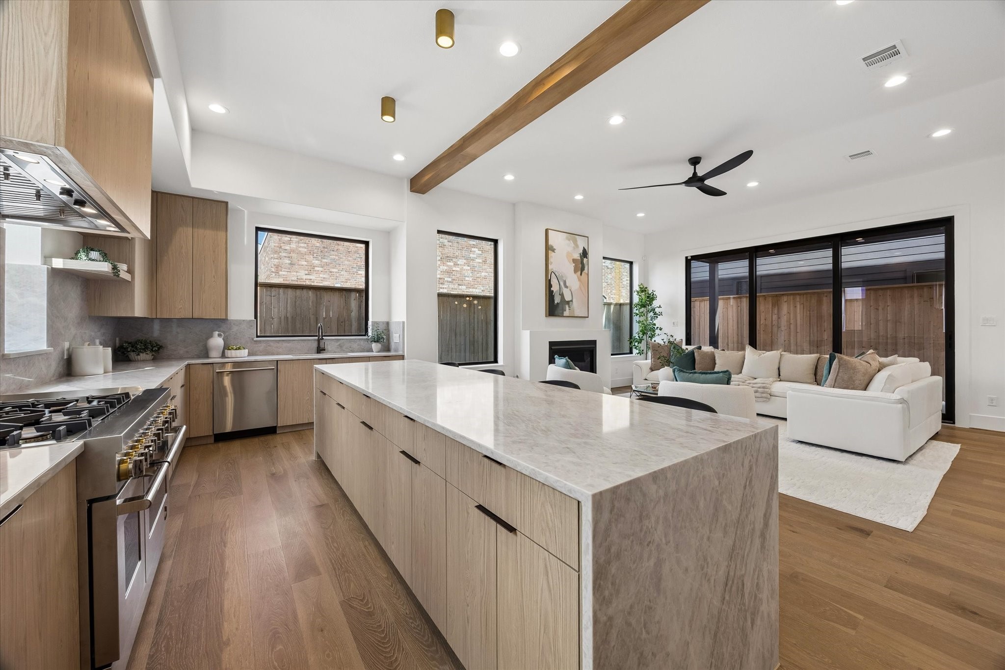 Designed as the heart of the home, the kitchen opens directly to the living area while a substantial wood ceiling beam creates subtle architectural separation. Wide sightlines and oversized windows keep both spaces visually connected and filled with natural light.