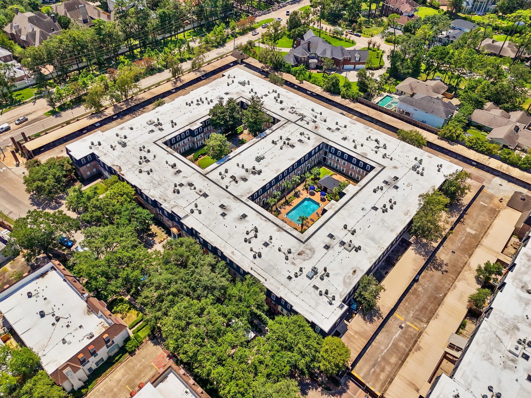 Expansive aerial view of a U-shaped residential complex featuring a central courtyard with a sparkling pool, surrounded by lush greenery and offering easy access to nearby amenities.
