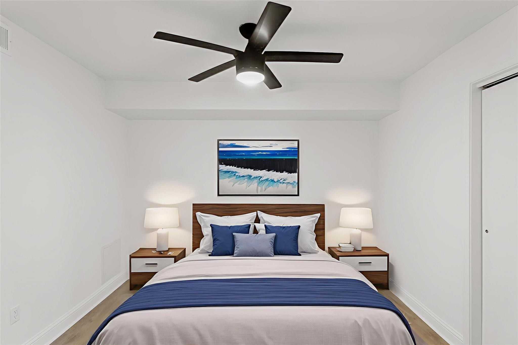 Modern bedroom featuring a stylish ceiling fan, cozy bed with blue accents, and elegant bedside tables with lamps for a serene ambiance.