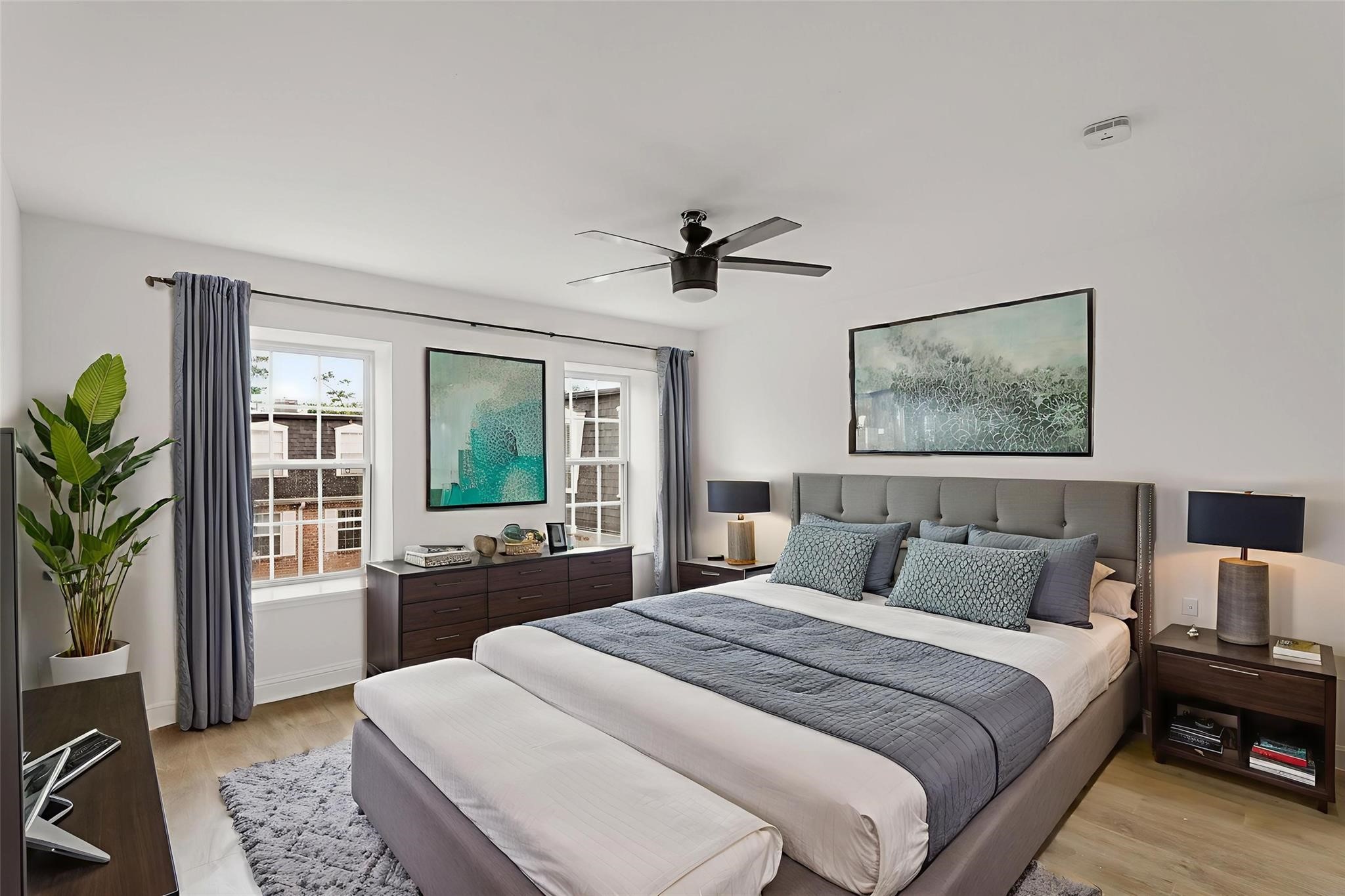 Spacious bedroom with a modern design, featuring a plush bed, stylish artwork, and ample natural light from large windows.