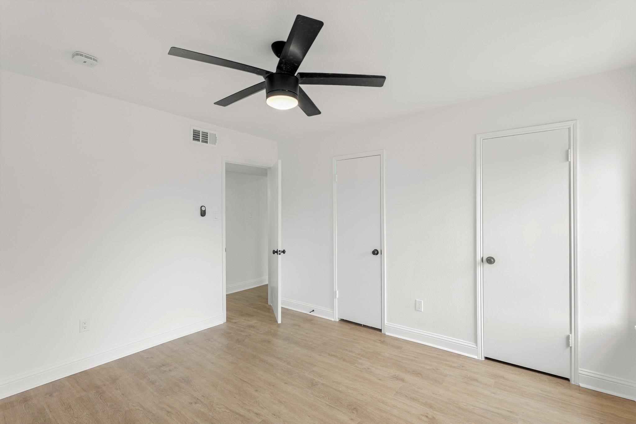 Bright, airy room featuring sleek laminate flooring, a modern black ceiling fan, and crisp white walls, perfect for a minimalist touch.