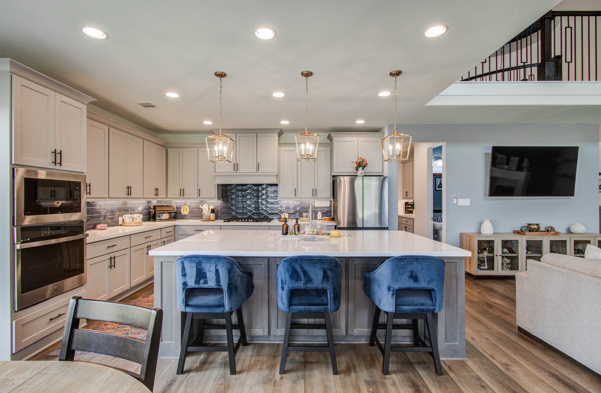 Experience modern living in this open-concept kitchen featuring a spacious island with seating for three, seamlessly flowing into a cozy living area with a wall-mounted TV.