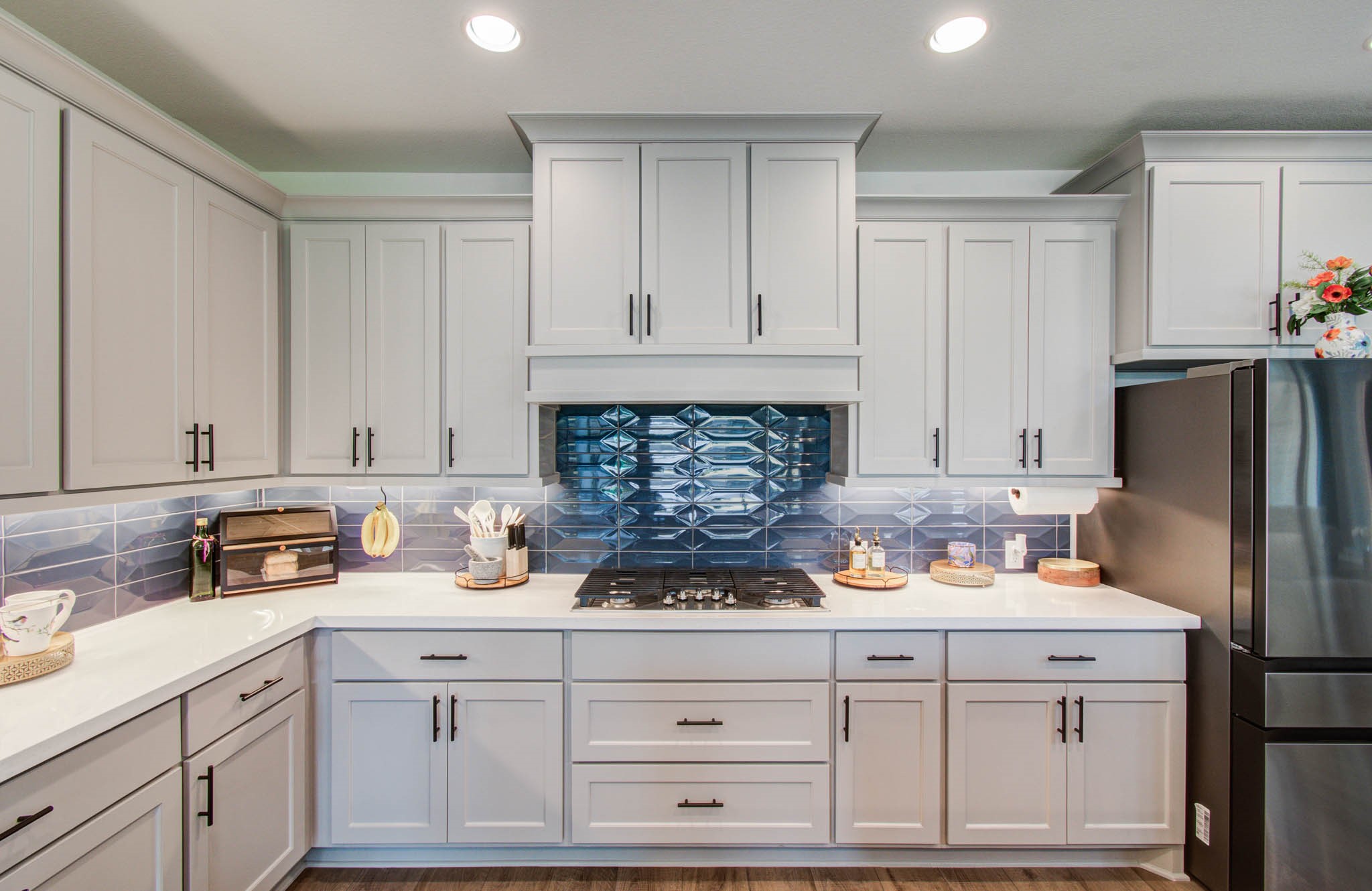 This modern kitchen features sleek white cabinetry, a striking blue geometric tile backsplash, and stainless steel appliances. The space is well-lit with recessed lighting and offers ample counter space for cooking and entertaining.