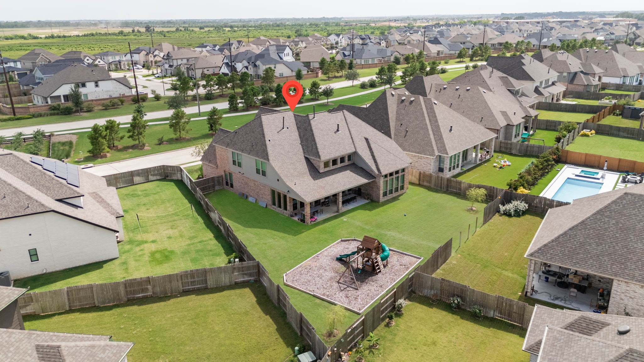 This aerial photo showcases a spacious, fenced backyard with a playset, offering a large lawn area. The home features a modern roof design, and the neighborhood is filled with similar, well-maintained houses, indicating a vibrant community.