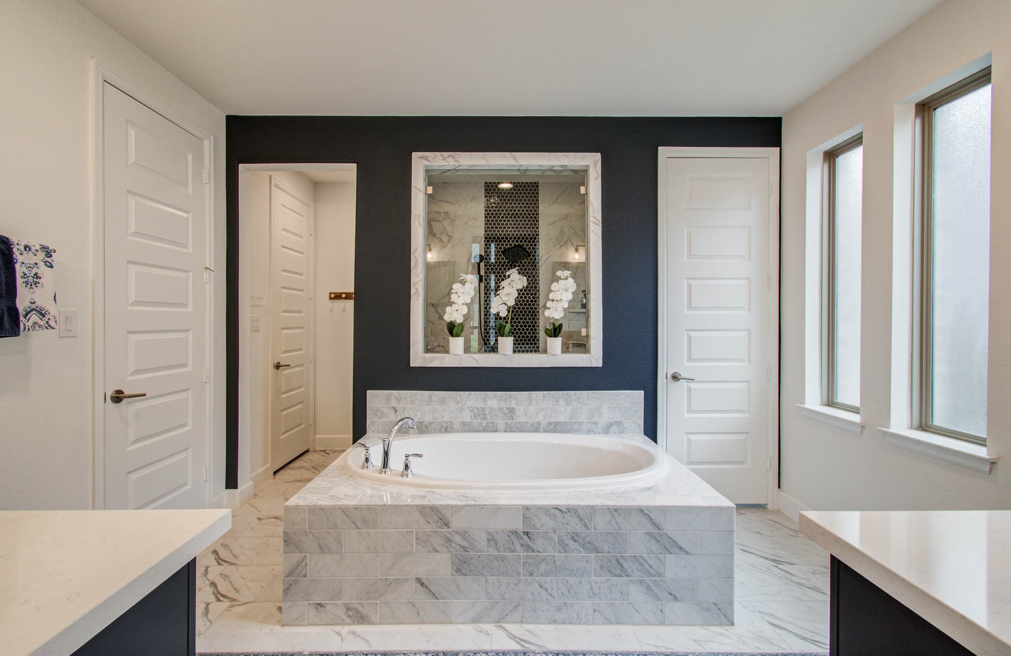 A luxurious marble tub takes center stage against a striking dark accent wall, enhanced by abundant natural light from large windows, creating a spacious and elegant modern bathroom.
