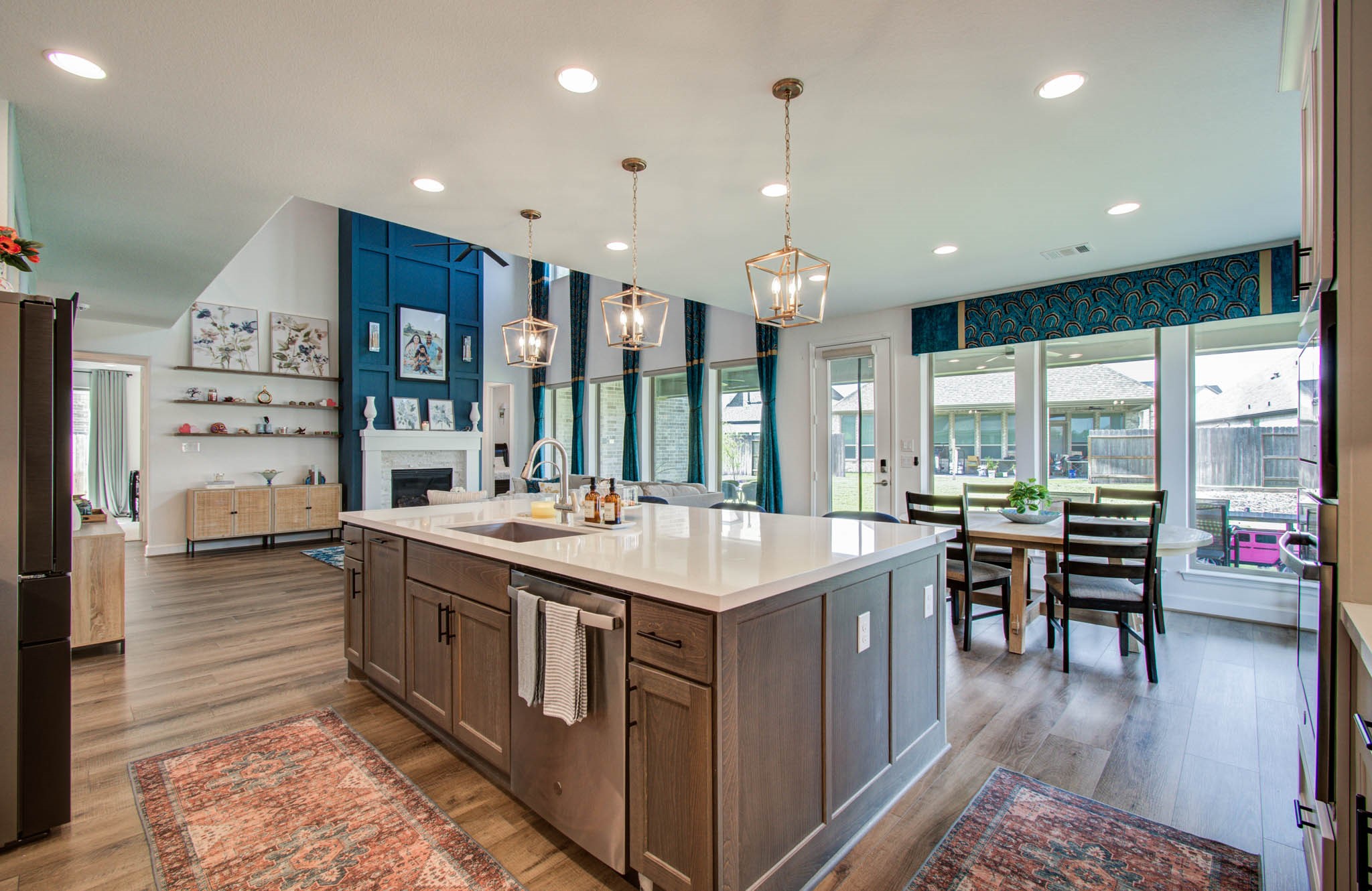 Experience the grandeur of a high-ceilinged living area accentuated by a bold blue wall with a cozy fireplace, bathed in natural light from large windows offering serene views of the fenced backyard.