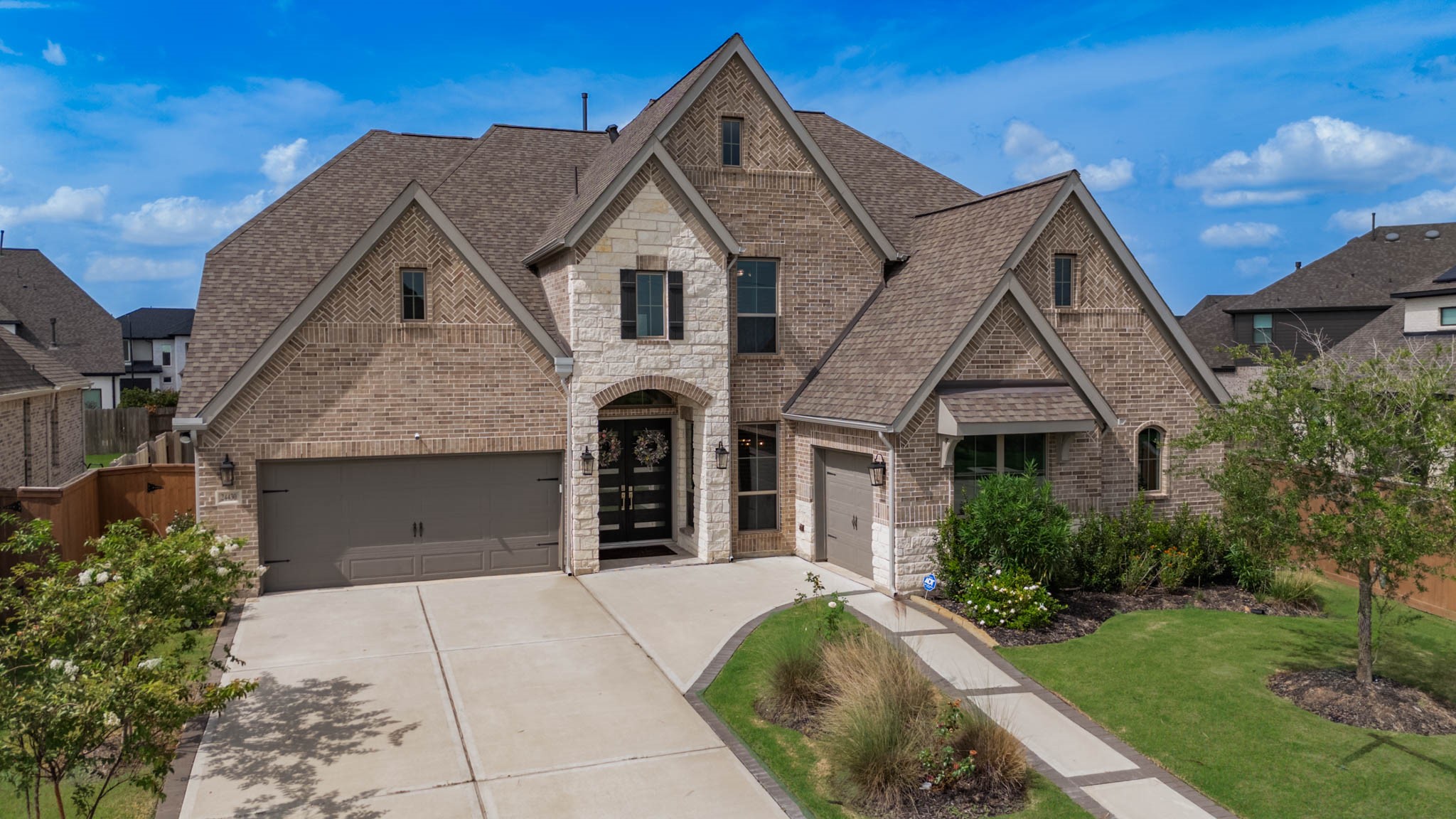 Charming two-story brick home with modern design, featuring a spacious driveway, two-car garage, and well-maintained landscaping, all highlighted by an inviting stone and brick entryway.