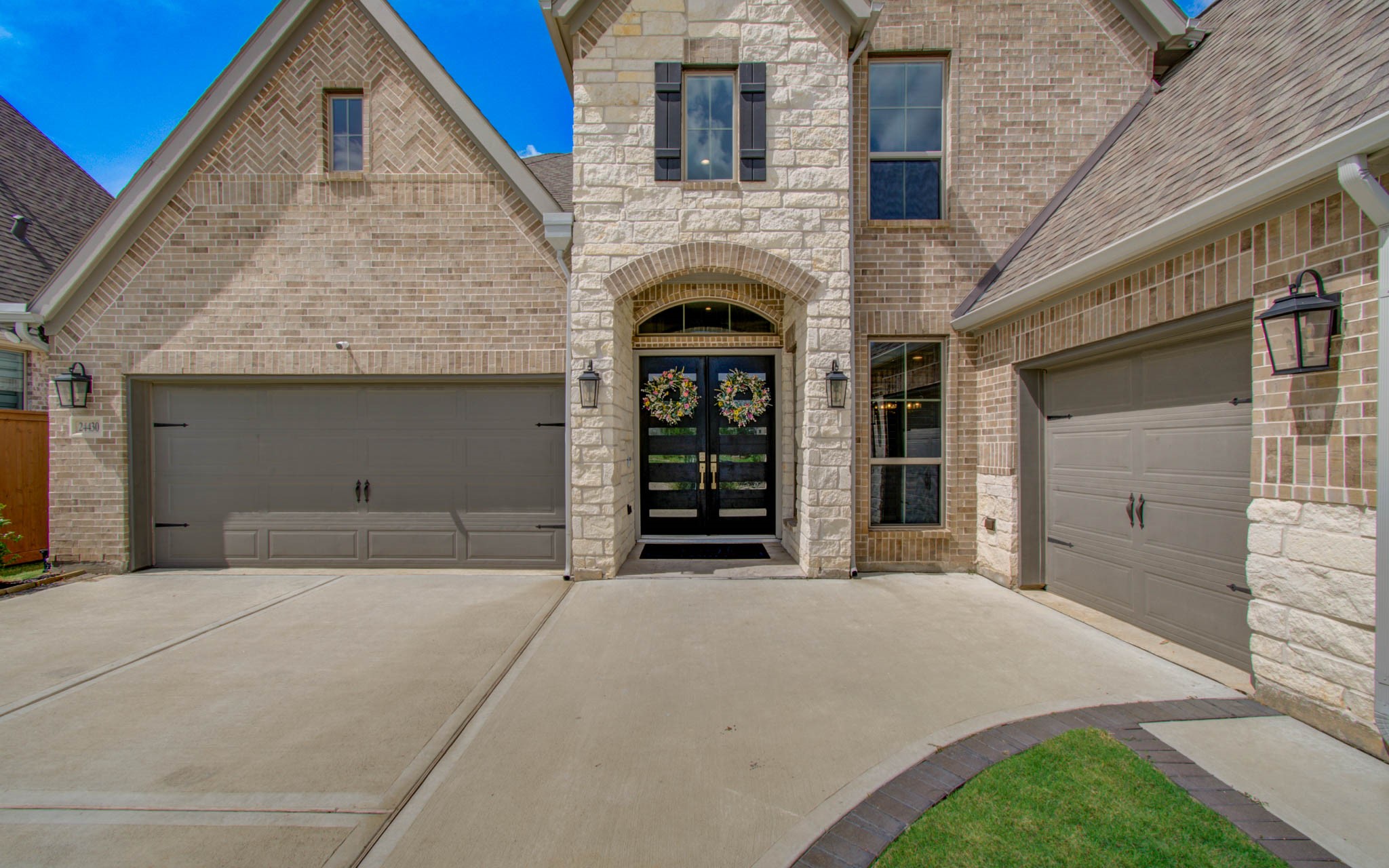 Discover elegance at 24430 Switchgrass Valley Way, featuring a stunning stone and brick facade with charming double doors and a spacious three-car garage.