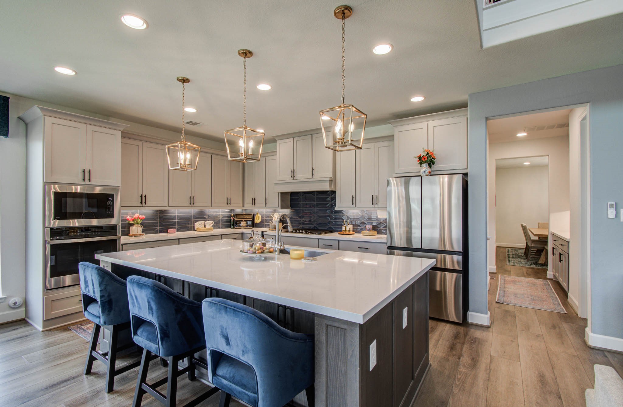 Discover a welcoming and functional kitchen featuring a spacious island with seating, elegant pendant lighting, stainless steel appliances, and sleek cabinetry, all enhanced by an open layout and soothing neutral tones.