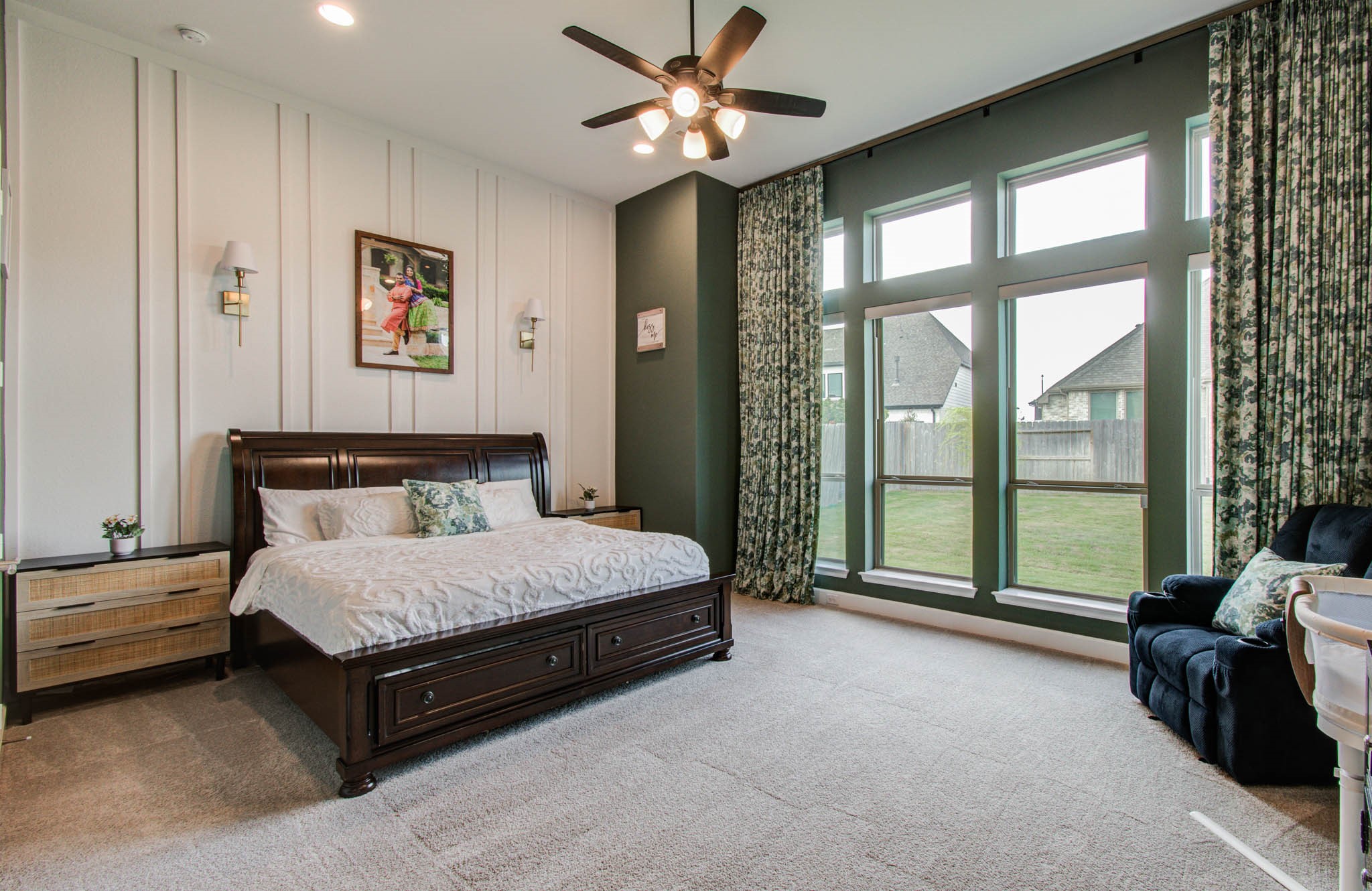 This spacious bedroom features large windows providing ample natural light, elegant paneled walls, and a ceiling fan. Welcoming and comfortable atmosphere.