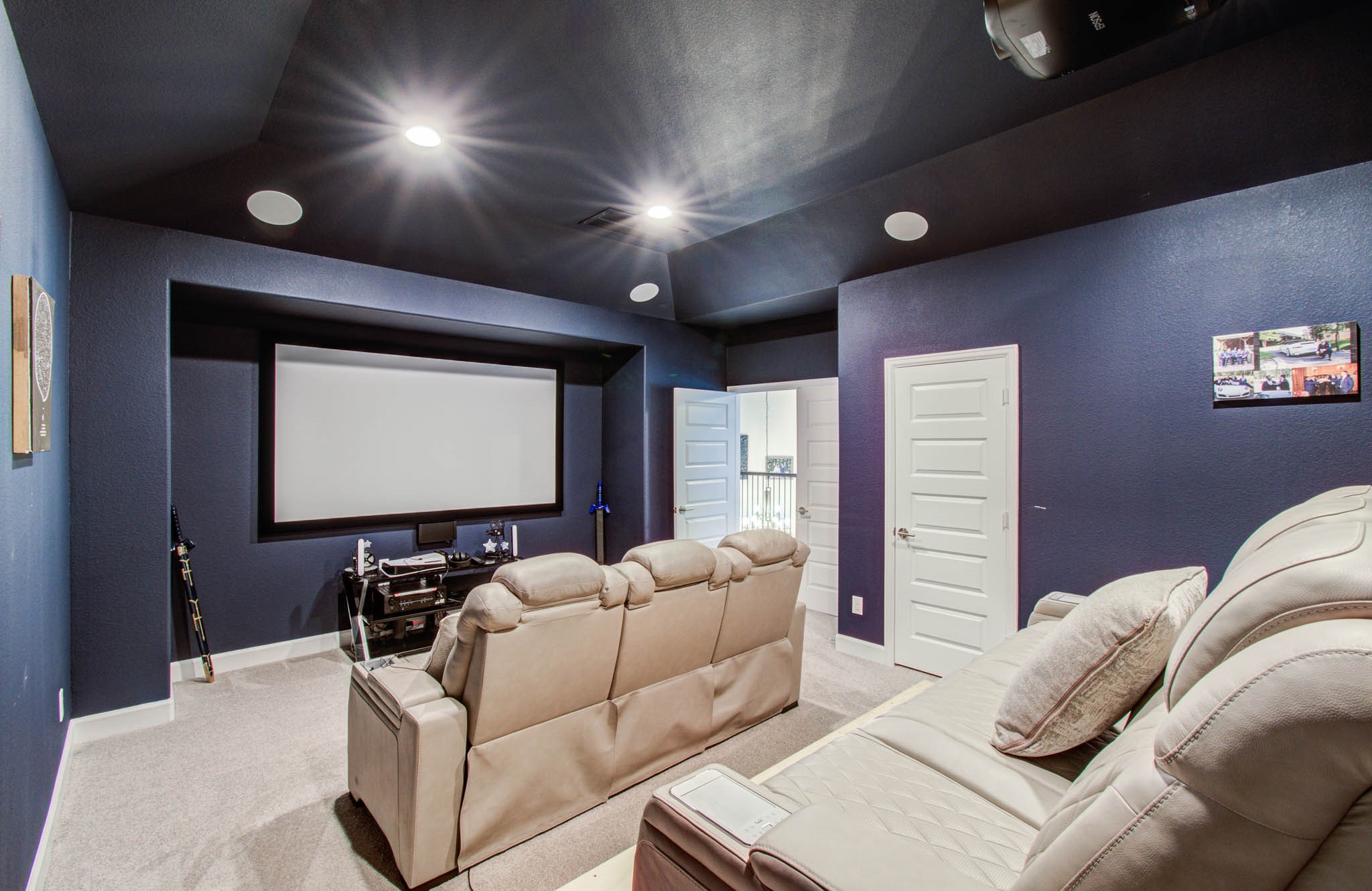 Experience ultimate movie nights in this cozy, soundproof home theater with navy blue walls, featuring plush leather seating, a built-in projector, and a mounted screen, all illuminated by sleek ceiling lights.