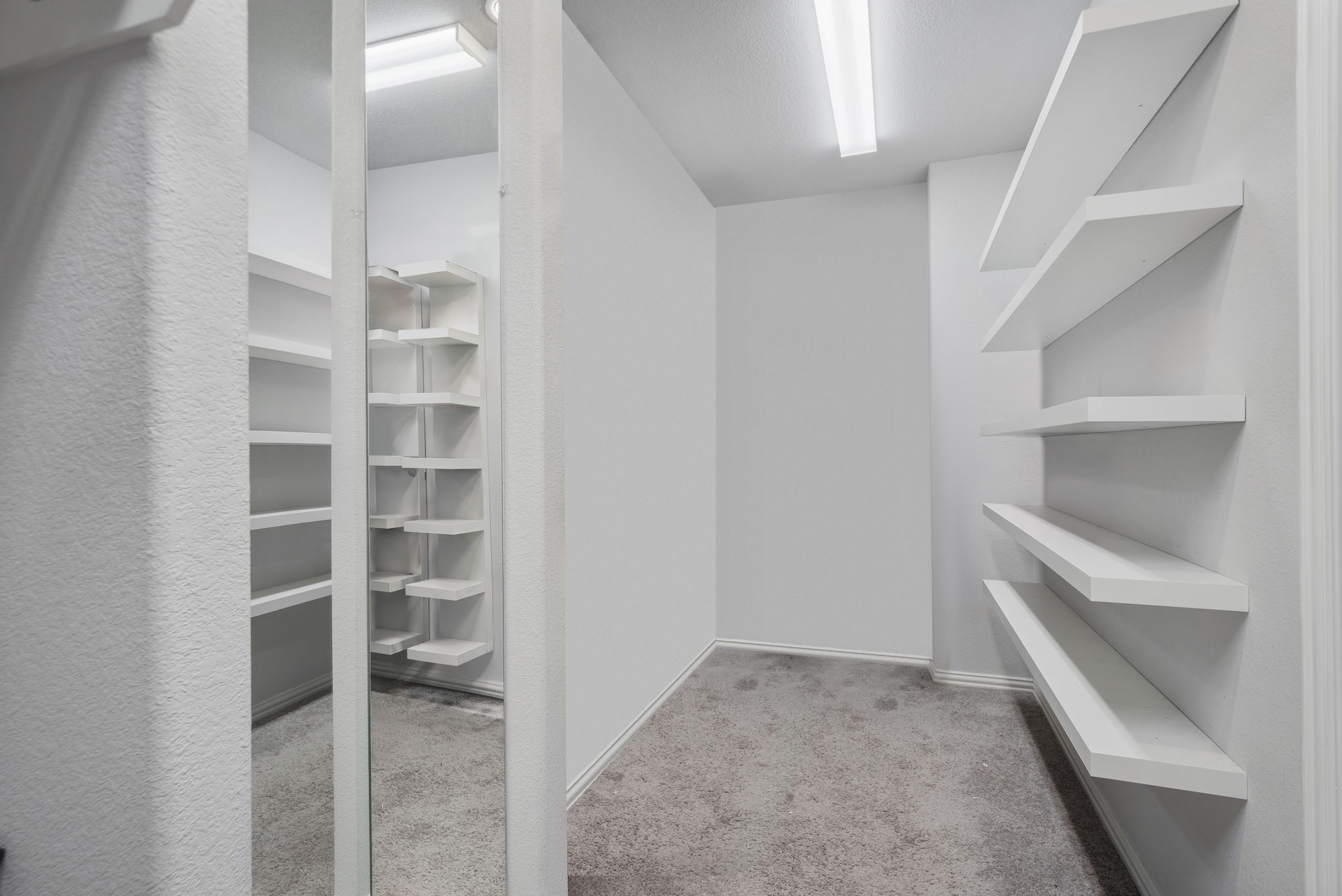 Primary walk-in spacious closet with custom shelves and mirrors.