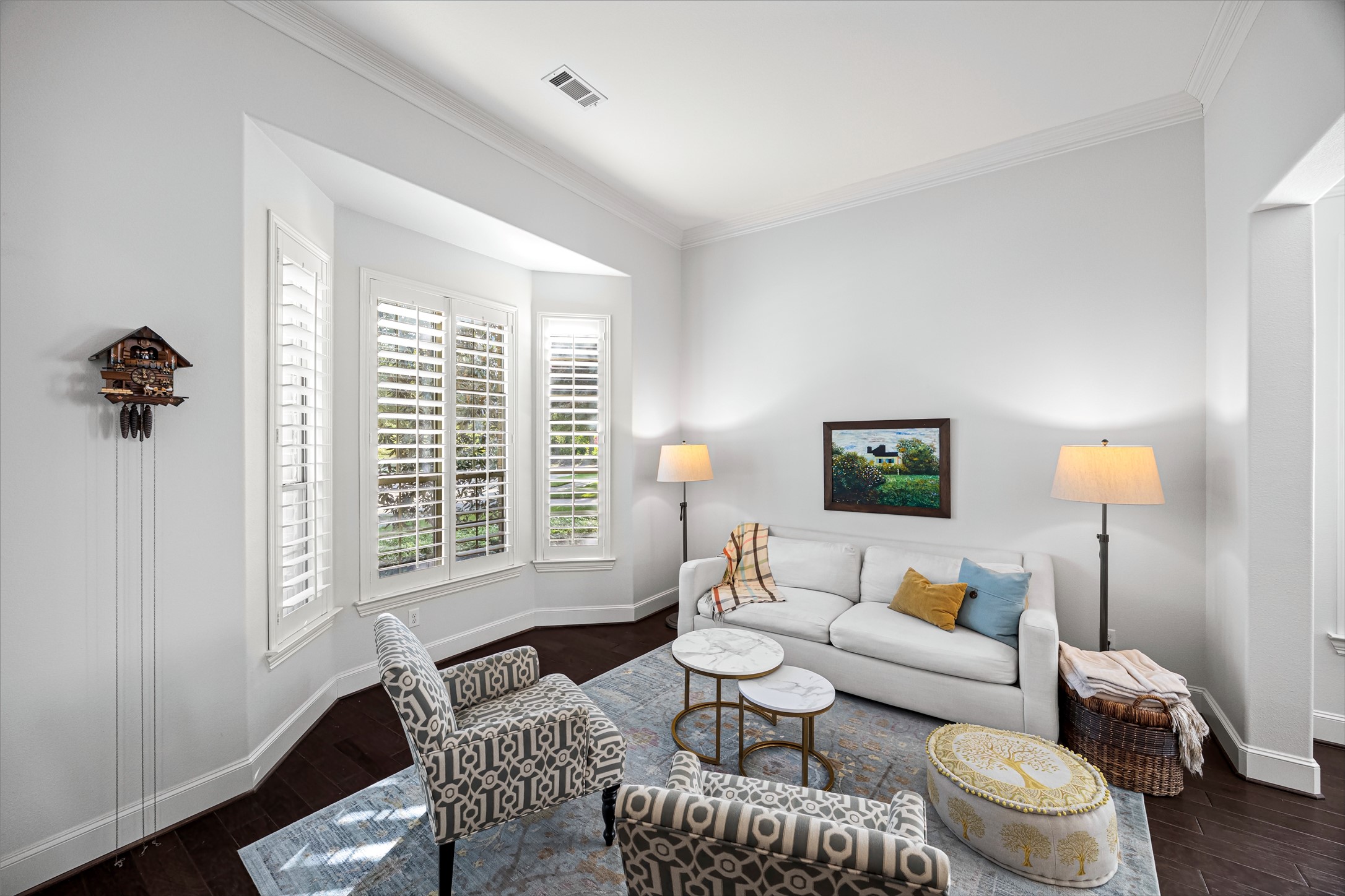 Light-filled sitting area with plantation shutters, crisp neutral palette, and rich dark flooring. New windows (2024). All new lighting on dimmers.