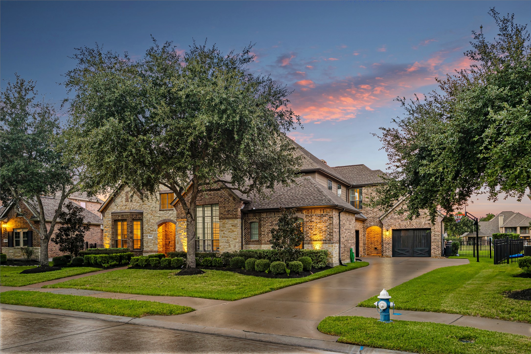 Elegant curb appeal with sweeping driveway, lush lawn, and mature tree canopy. New windows (2024). (Virtually enhanced: driveway reflection)
