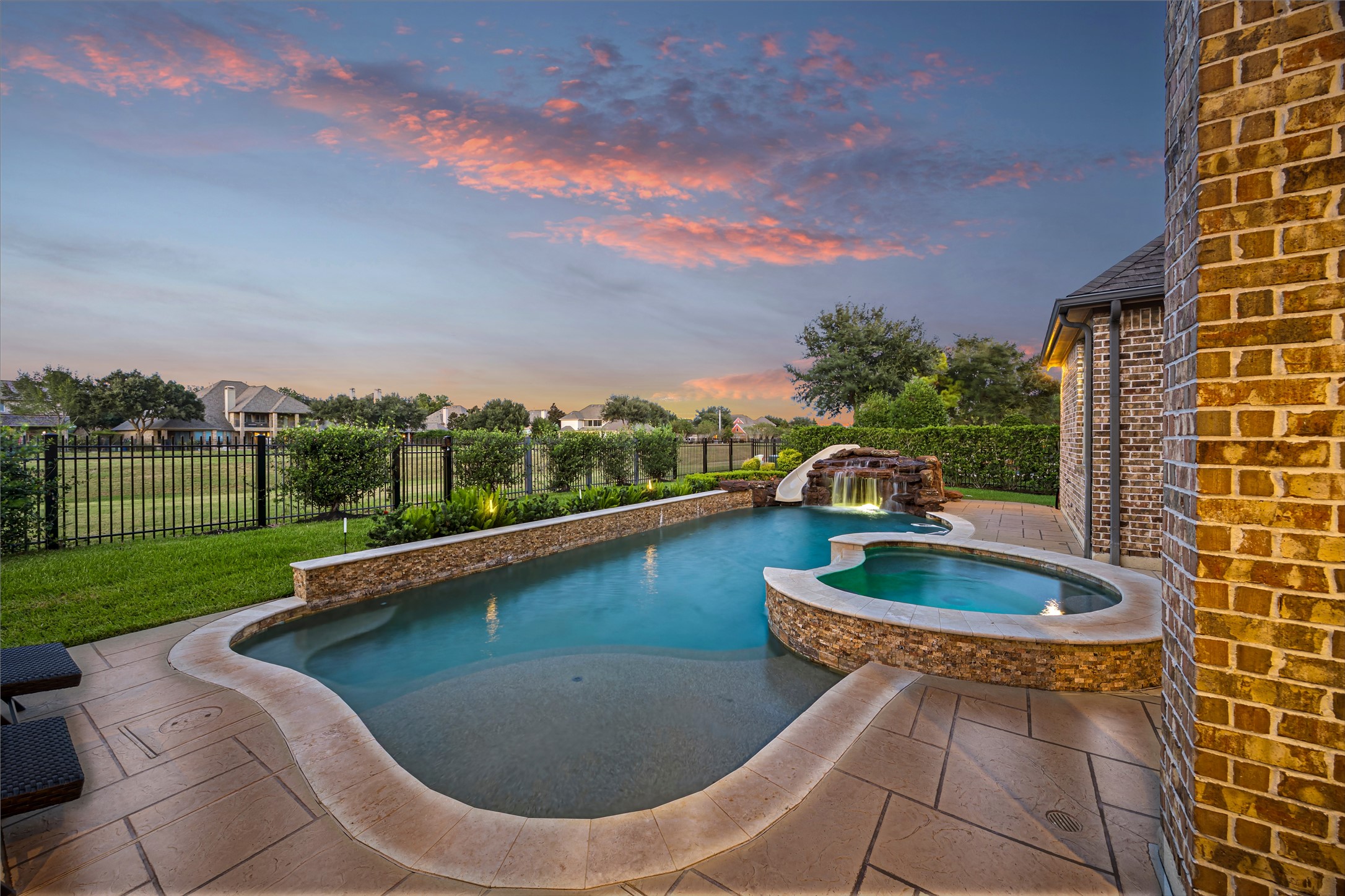 Pool and spa glowing at twilight against the backyard landscape. Heated PebbleTec chlorine pool.