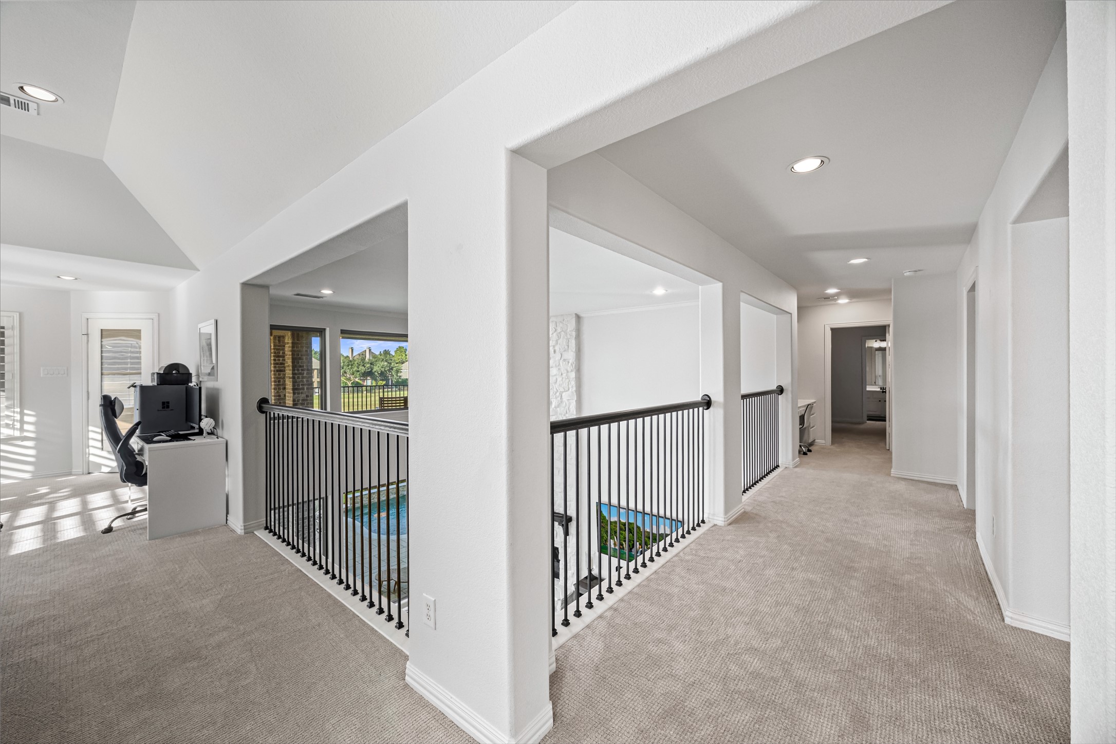 Upstairs landing with wrought-iron railing overlooking the main level, recessed lighting, and plush carpet, connecting to the secondary bedrooms and a built-in office nook.