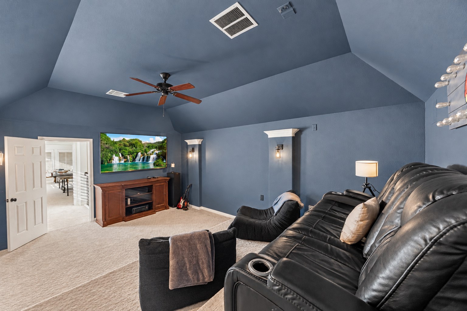 Media room with tray ceiling, ceiling fan, and generous space for theater-style seating. Built-in speakers in media room.
