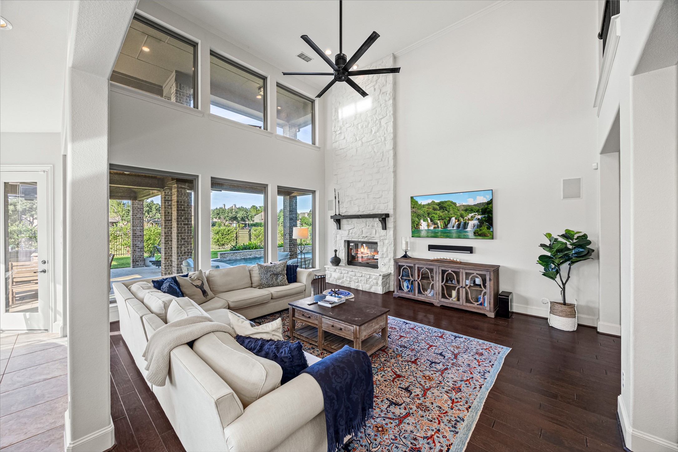 Showpiece living room with soaring ceilings, a wall of windows, and sweeping backyard views. New windows (2024). Built-in speakers and Big Ass Fan controlled by Nest.