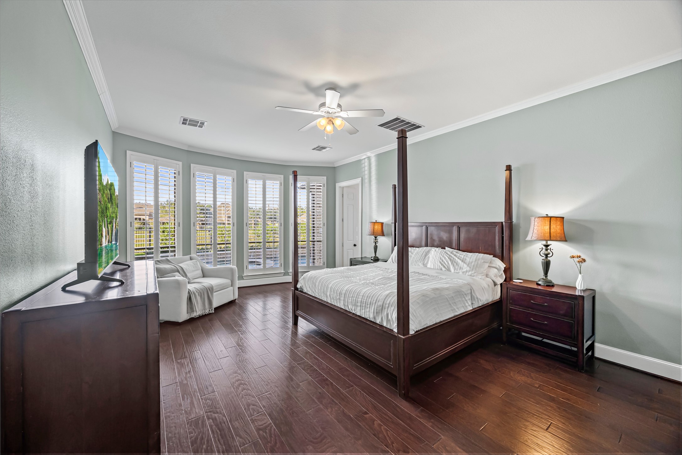 Spacious primary bedroom with large windows, ceiling fan, and rich dark flooring. New windows (2024). Updated paint throughout.