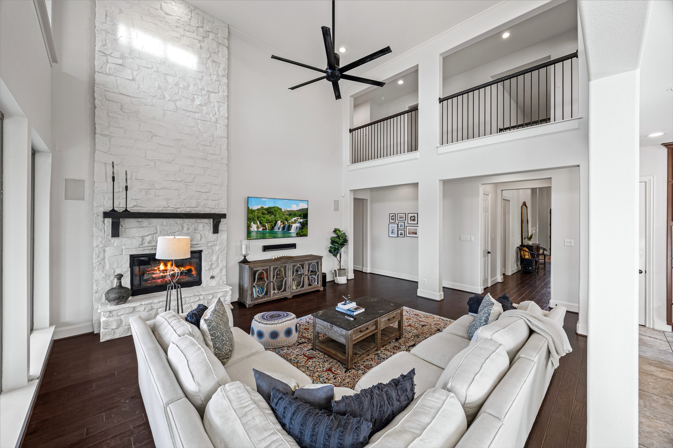 Expansive living room with high ceilings, ceiling fan, and an open, airy layout. Painted fireplace with updated stone, built-in speakers, and Big Ass Fan controlled by Nest.