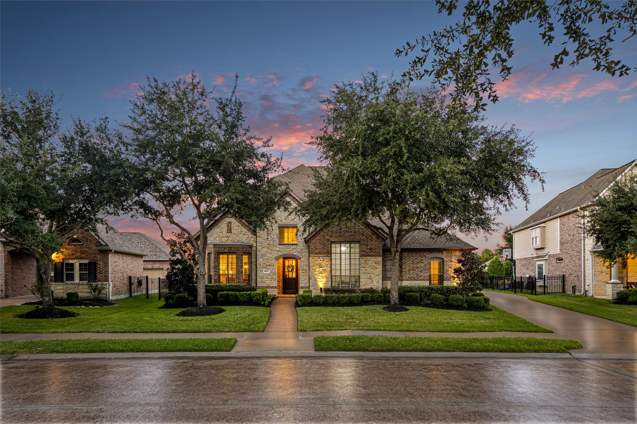 Stately brick and stone facade glowing at twilight, framed by towering mature oaks and manicured landscaping. New windows (2024). (Virtually enhanced: driveway reflection)