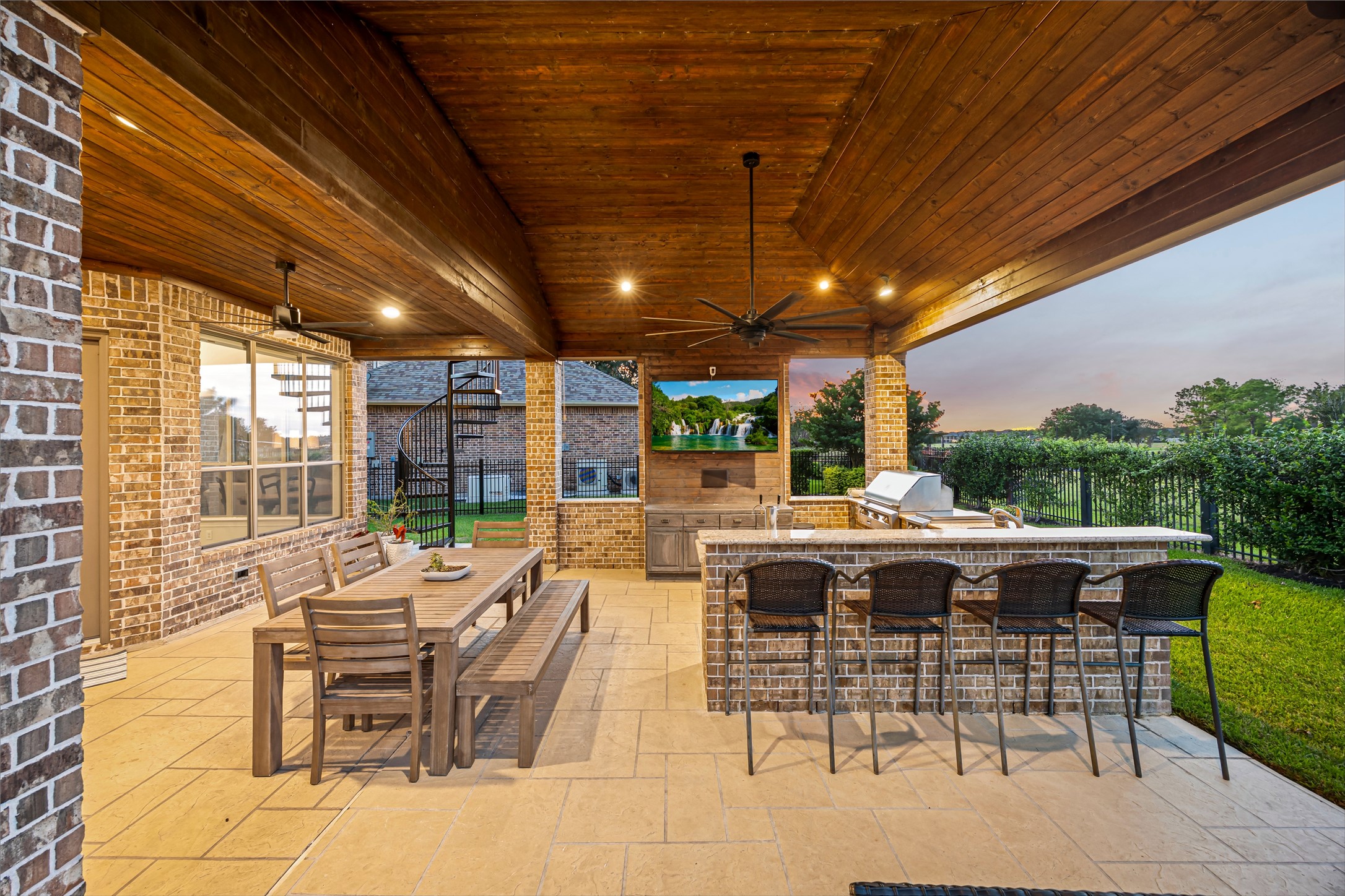 Covered outdoor living area with bar seating, outdoor kitchen, and stained wood ceiling. Great sunsets from the backyard bar. Alfresco grill and flat grill, ice maker, and exterior surround sound.
