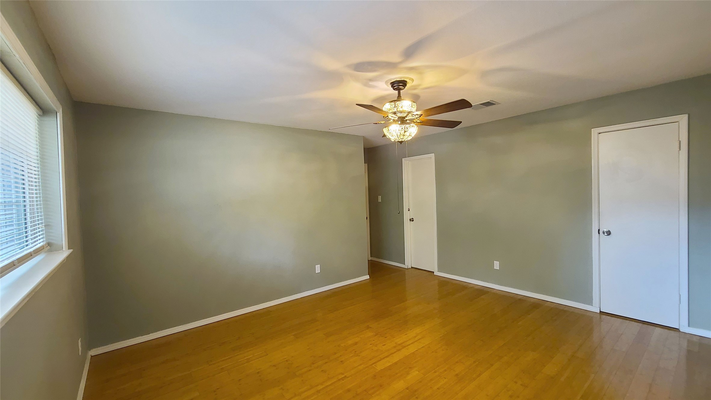 Discover a spacious bedroom featuring warm bamboo wood floors, a stylish ceiling fan, and soft natural light streaming through the window, creating a serene retreat.