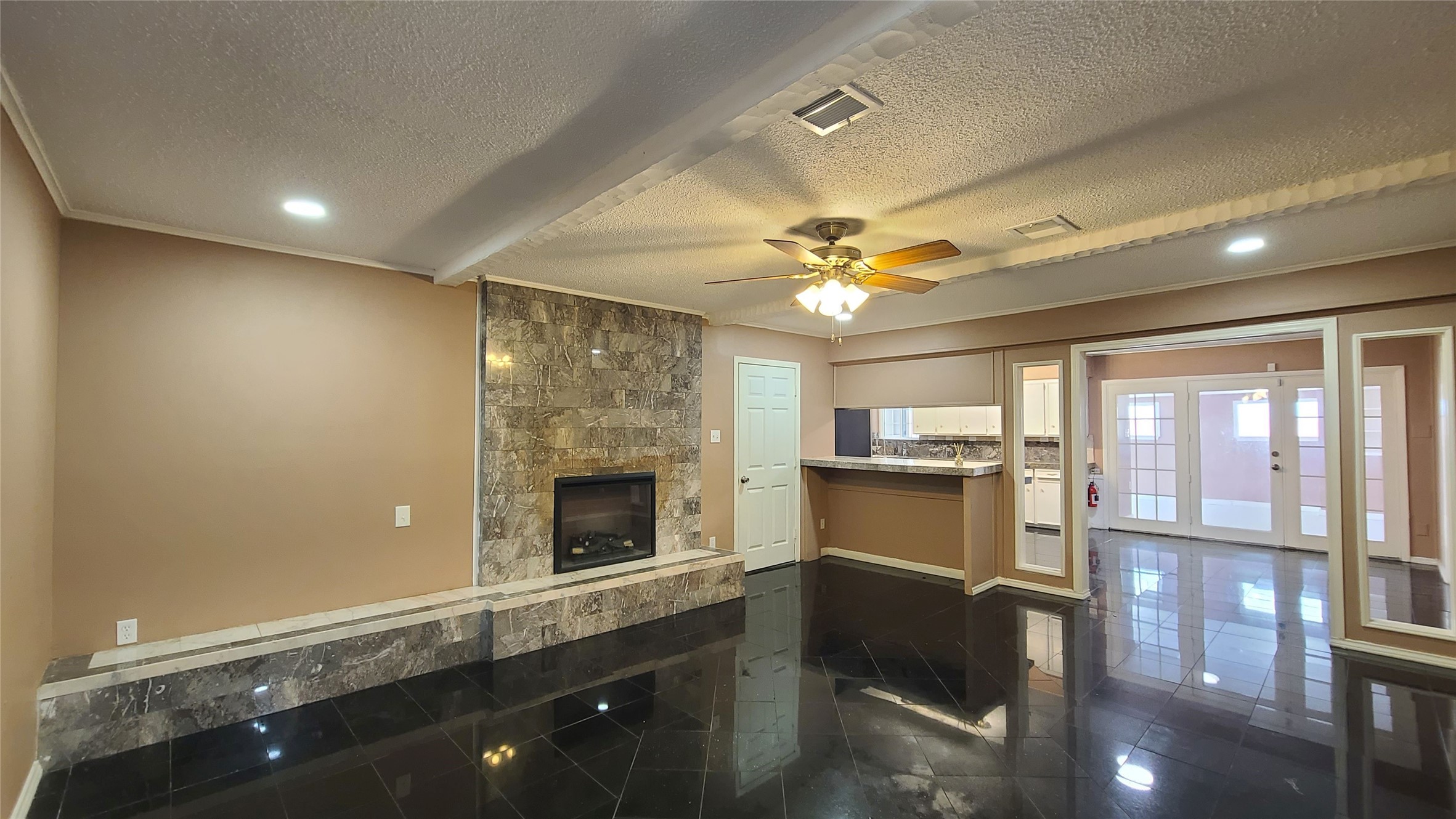 Spacious family room with elegant stone fireplace and glossy tile floors, seamlessly connected to the kitchen, with the convenience of a full bath vanity just behind for added functionality.