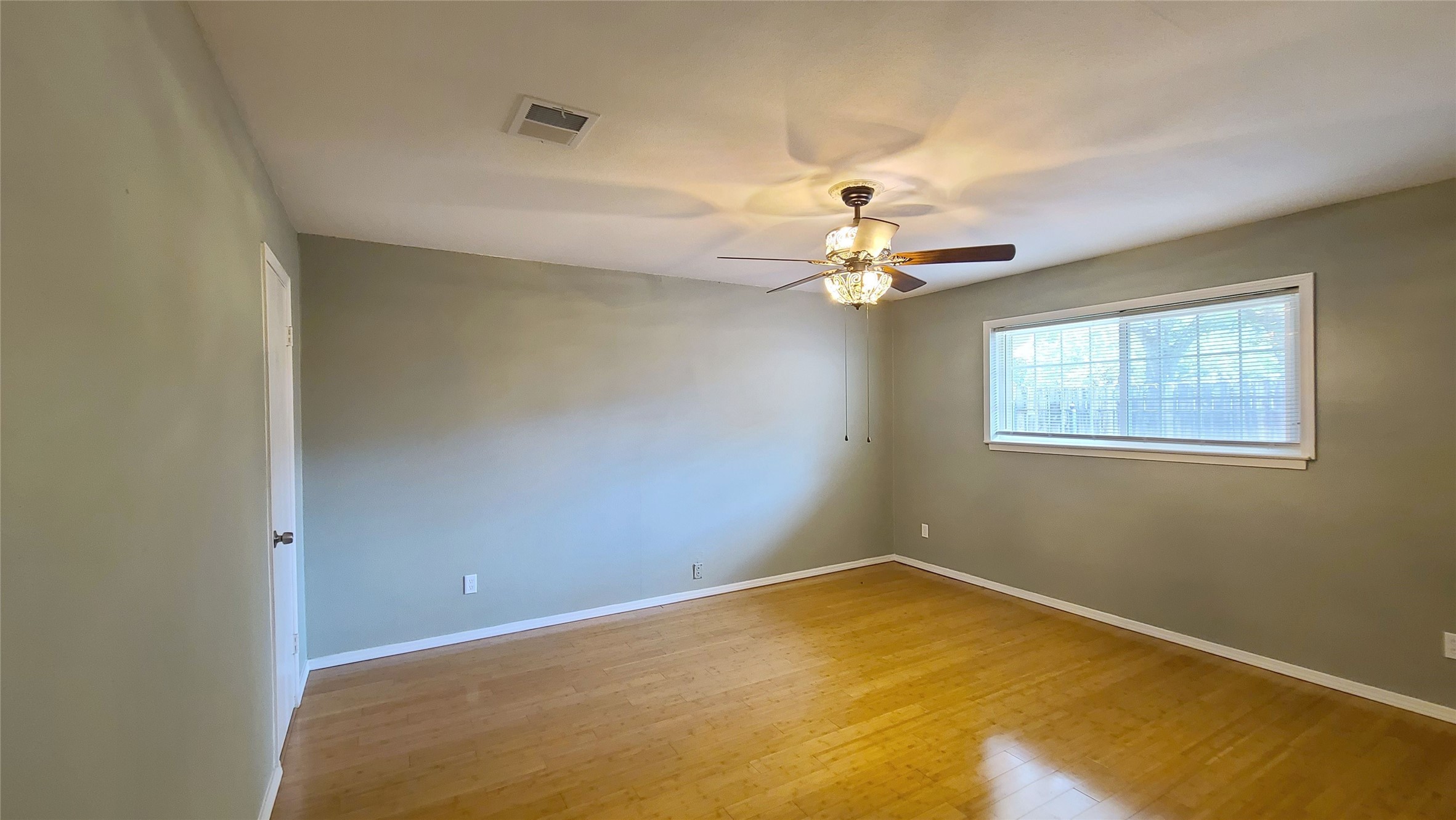 Bright and welcoming bedroom featuring sleek bamboo wood floors, ample closet space, and abundant natural light streaming through large windows for a serene and airy retreat.