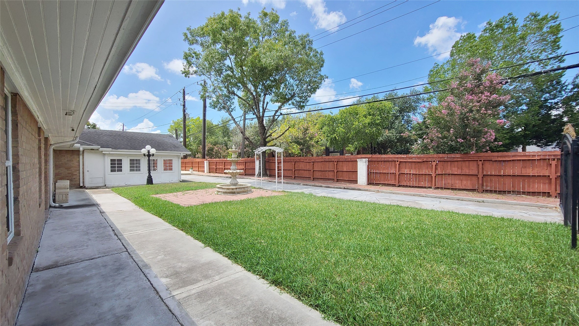 Charming single-story home with a classic brick exterior, featuring a welcoming courtyard with a central fountain and elegant lamppost, surrounded by lush greenery.