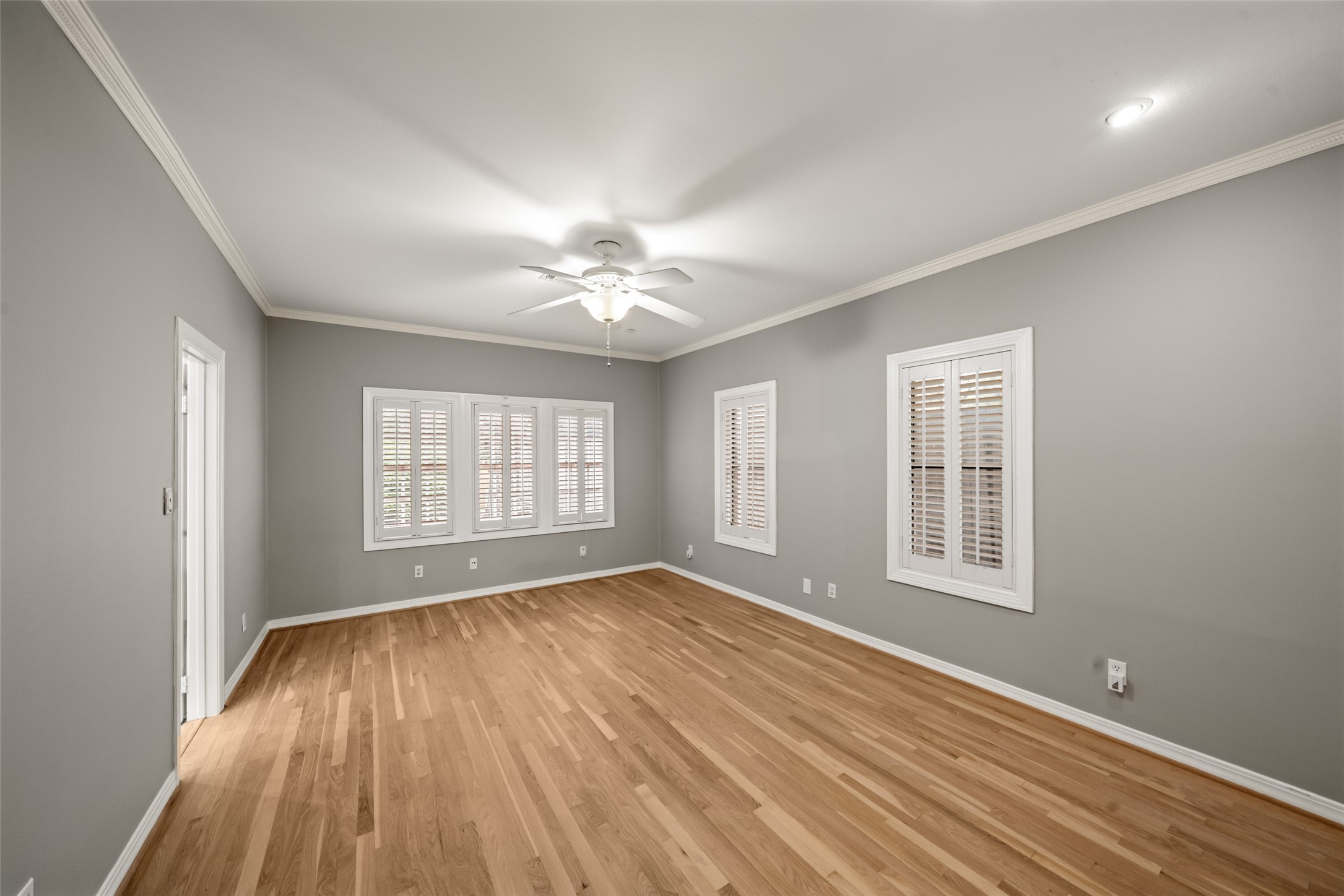 Spacious primary bedroom featuring wood floors, crown molding, and windows with shutters.