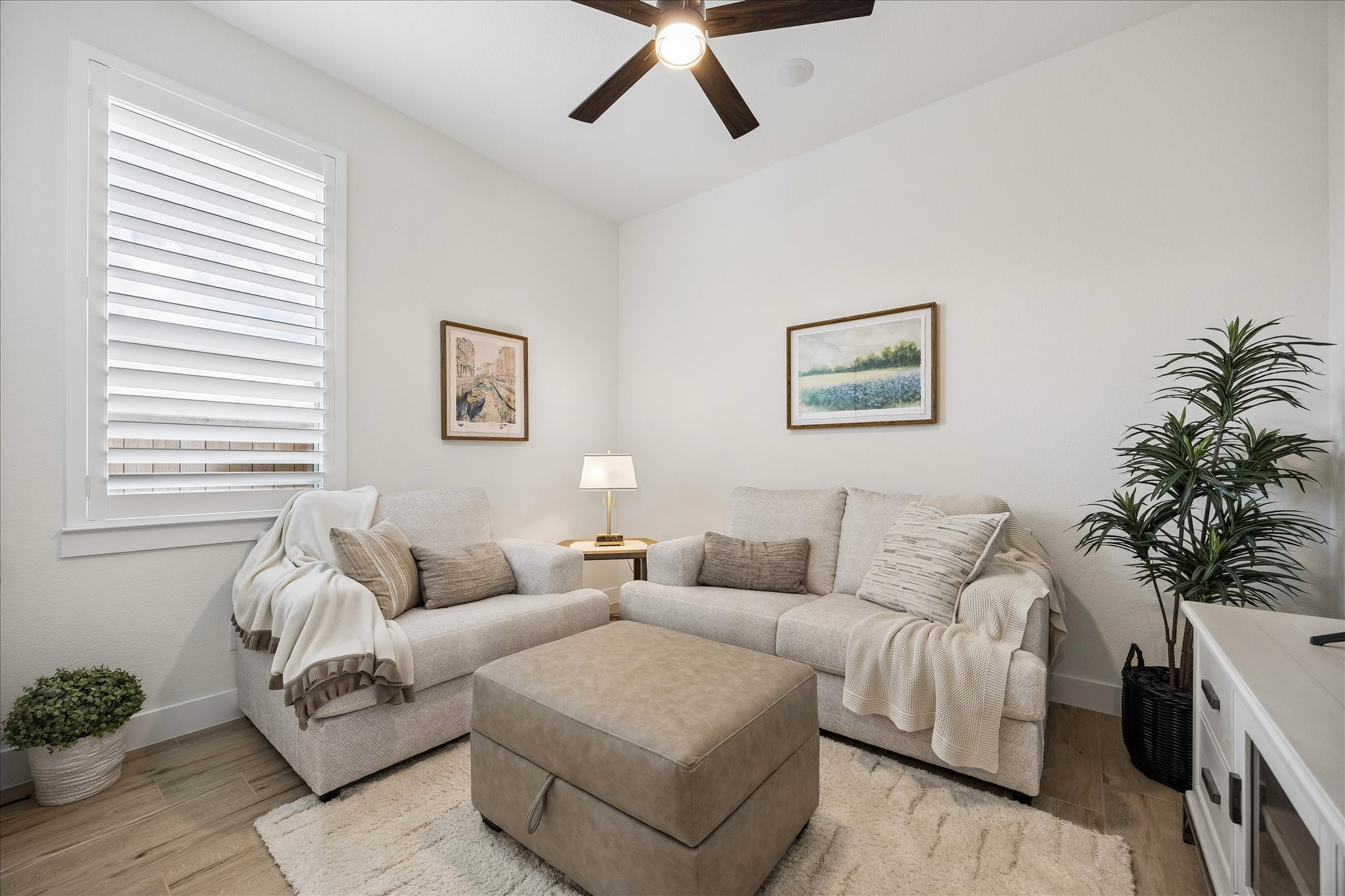 The second bedroom features custom plantation shutters, wood-plank tile flooring, and a ceiling fan. This versatile space is ideal as a guest room, childrens bedroom, hobby room, or entertainment area, as shown.