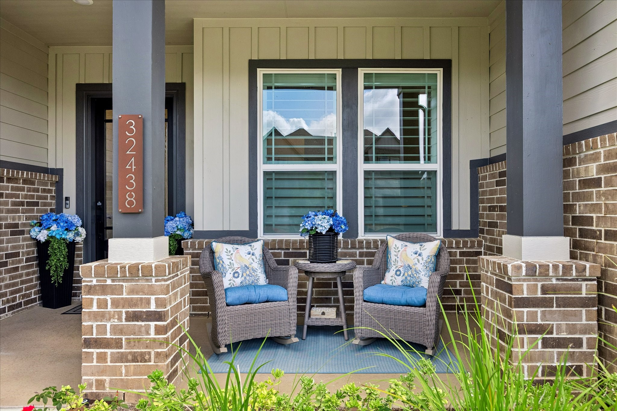 Covered front porch framed by painted Hardy siding and brick creates a warm architectural entry with clean lines and recessed lighting overhead. Glass pane mahogany front door allows natural light inside while maintaining a sence of privacy.