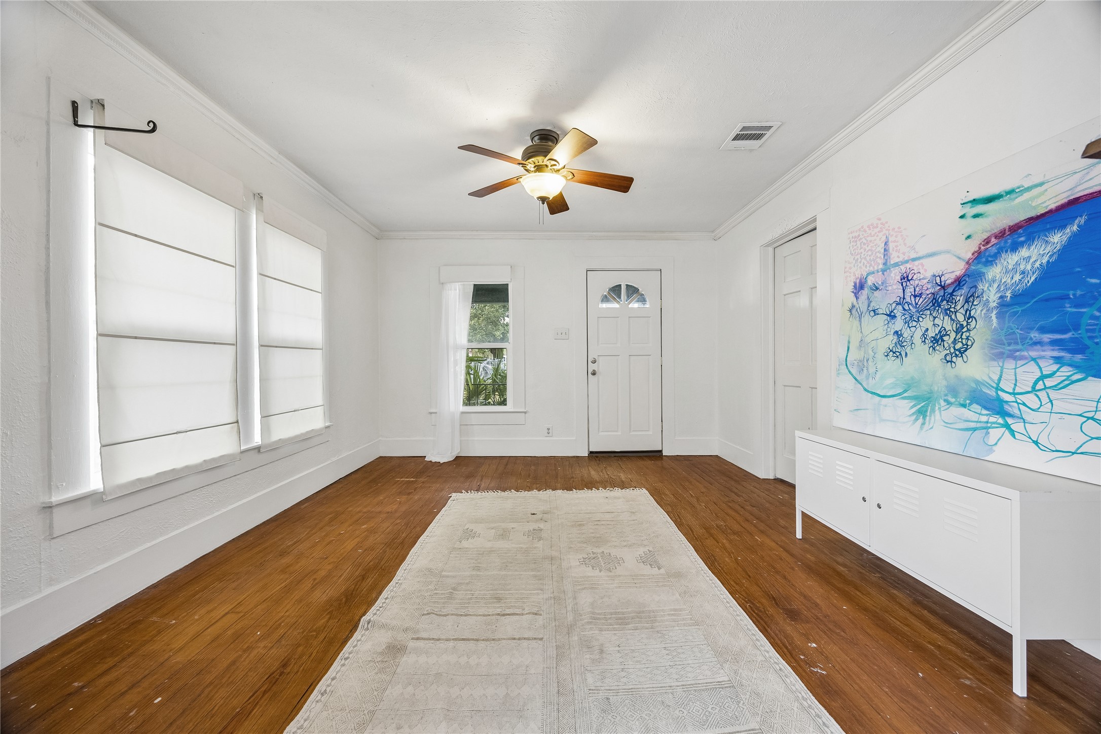 Step inside to a bright, inviting living space featuring warm wood floors, crisp white walls, abundant windows, and a ceiling fan for added comfort