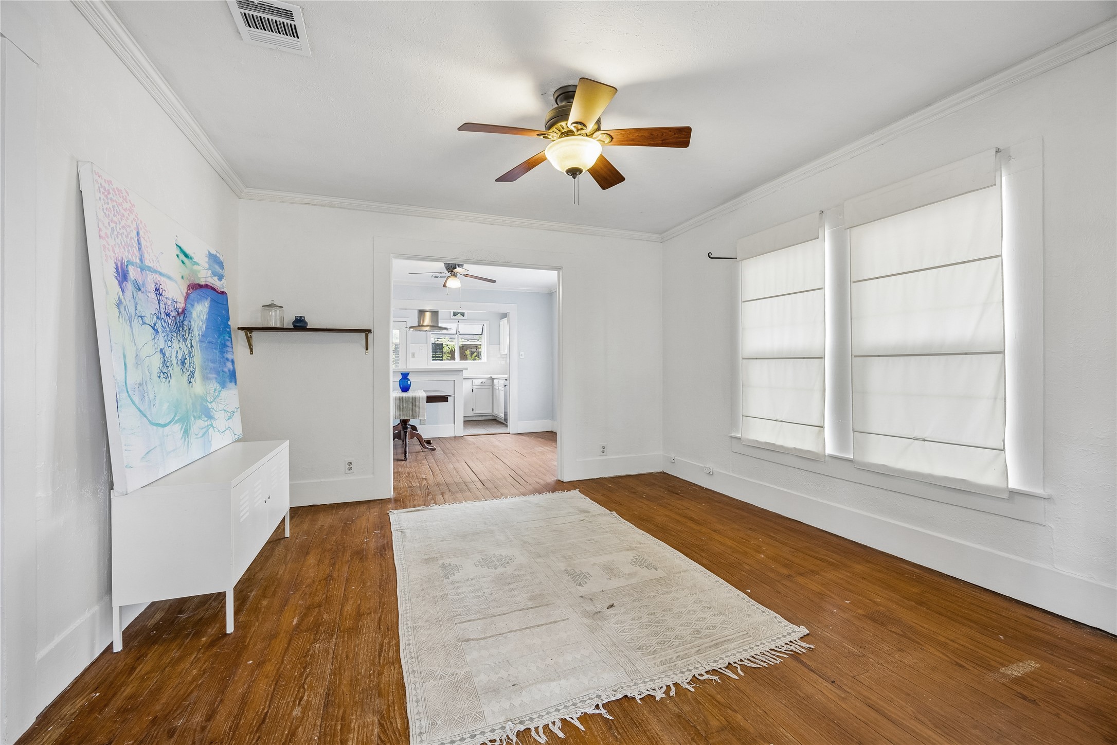 Opposing view of the spacious main living area which pairs beautiful wood flooring with tall windows and an easy flow into the adjoining dining and kitchen spaces, creating an open, connected feel.