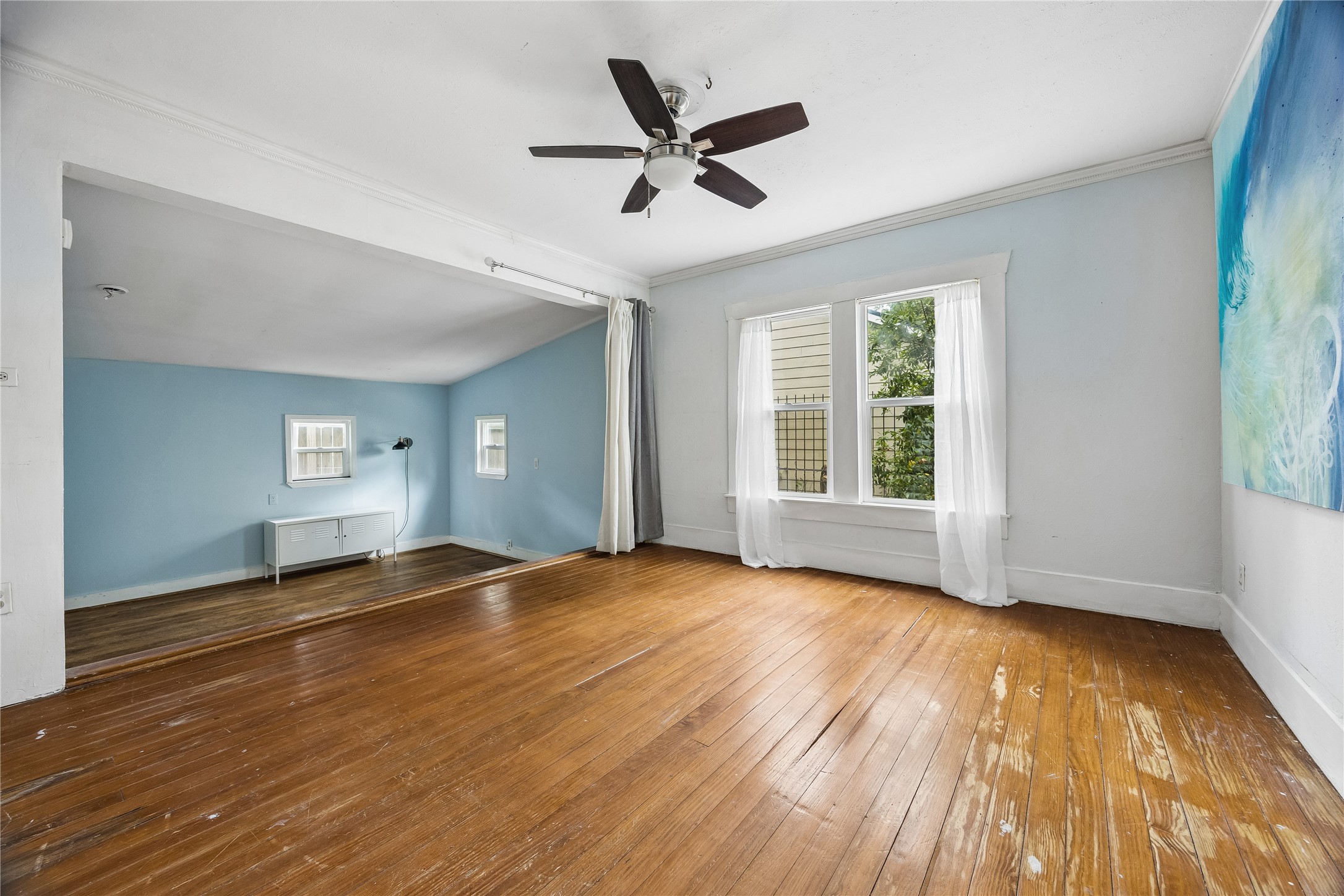 Natural light pours into this generously sized room, highlighting its wood floors, ceiling fan, and open connection to an additional flexible living area.